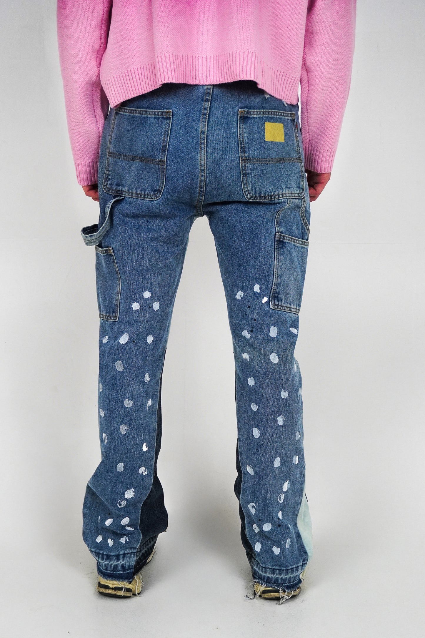 Blue jeans with white polka dots worn by a person in a pink sweater on a white background
