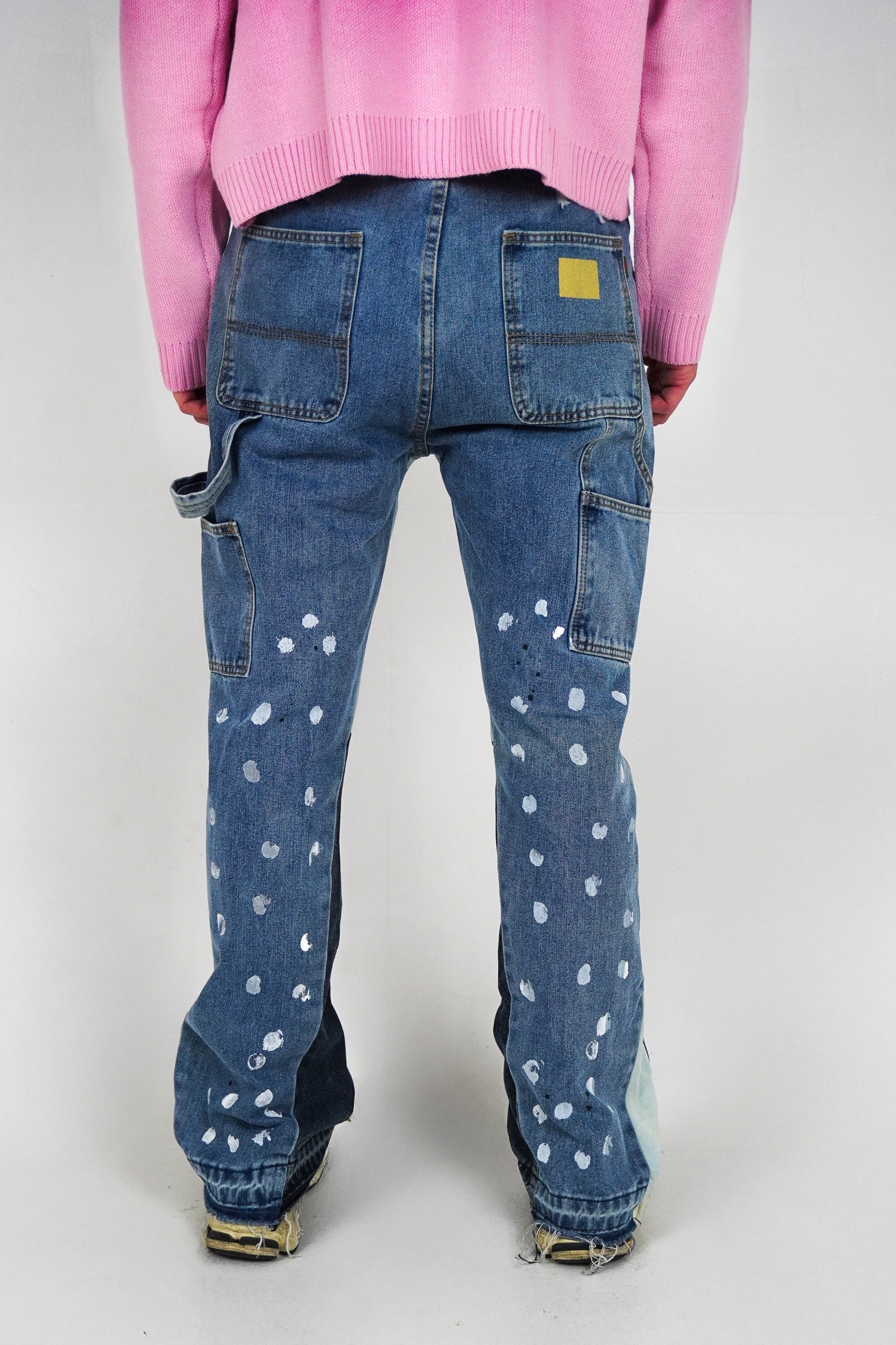 Blue jeans with white polka dots worn by a person in a pink sweater on a white background