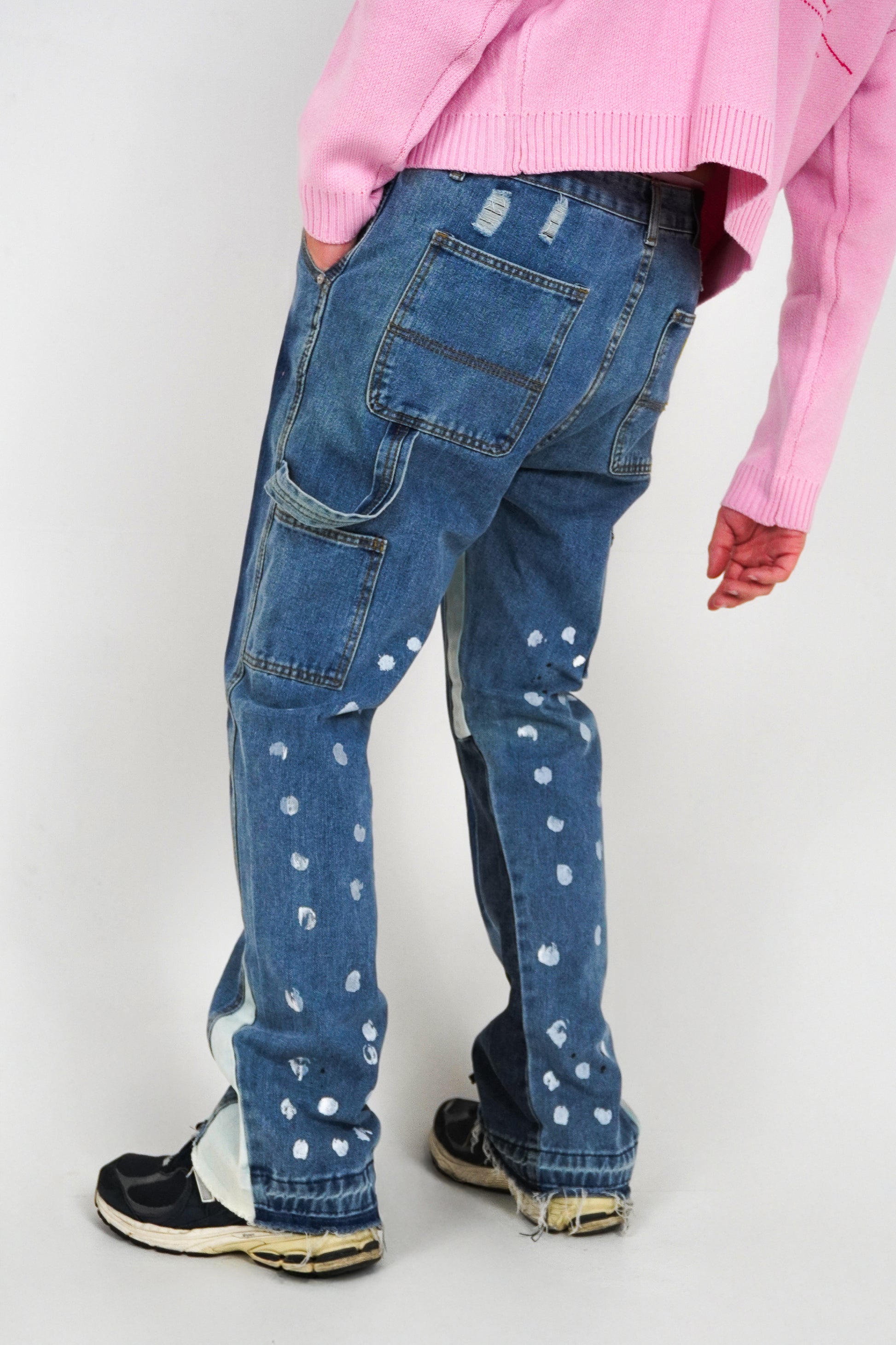 Person wearing blue jeans with white patterns and a pink sweater on a white background