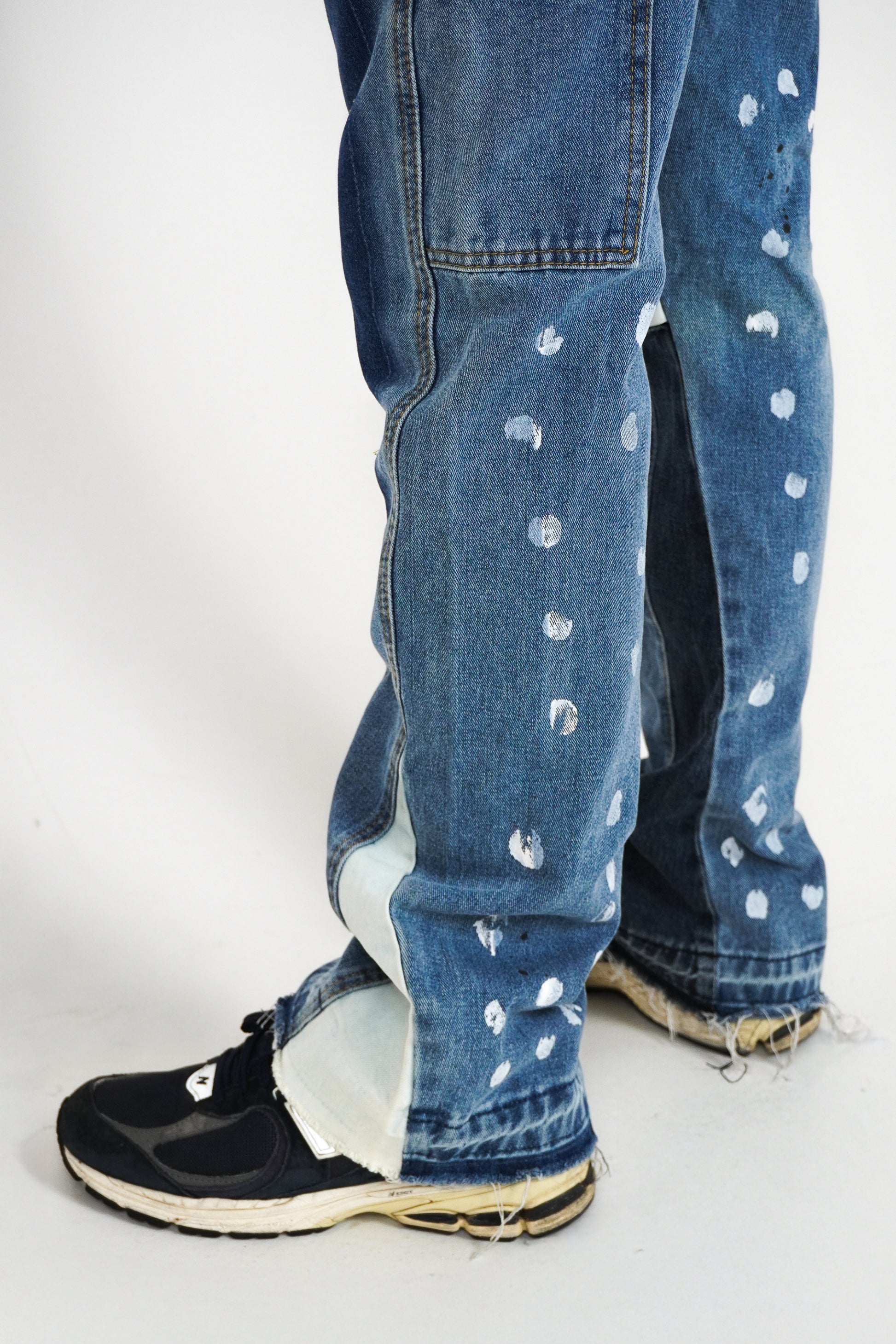 Blue jeans with white paint splashes worn by a person on a white background