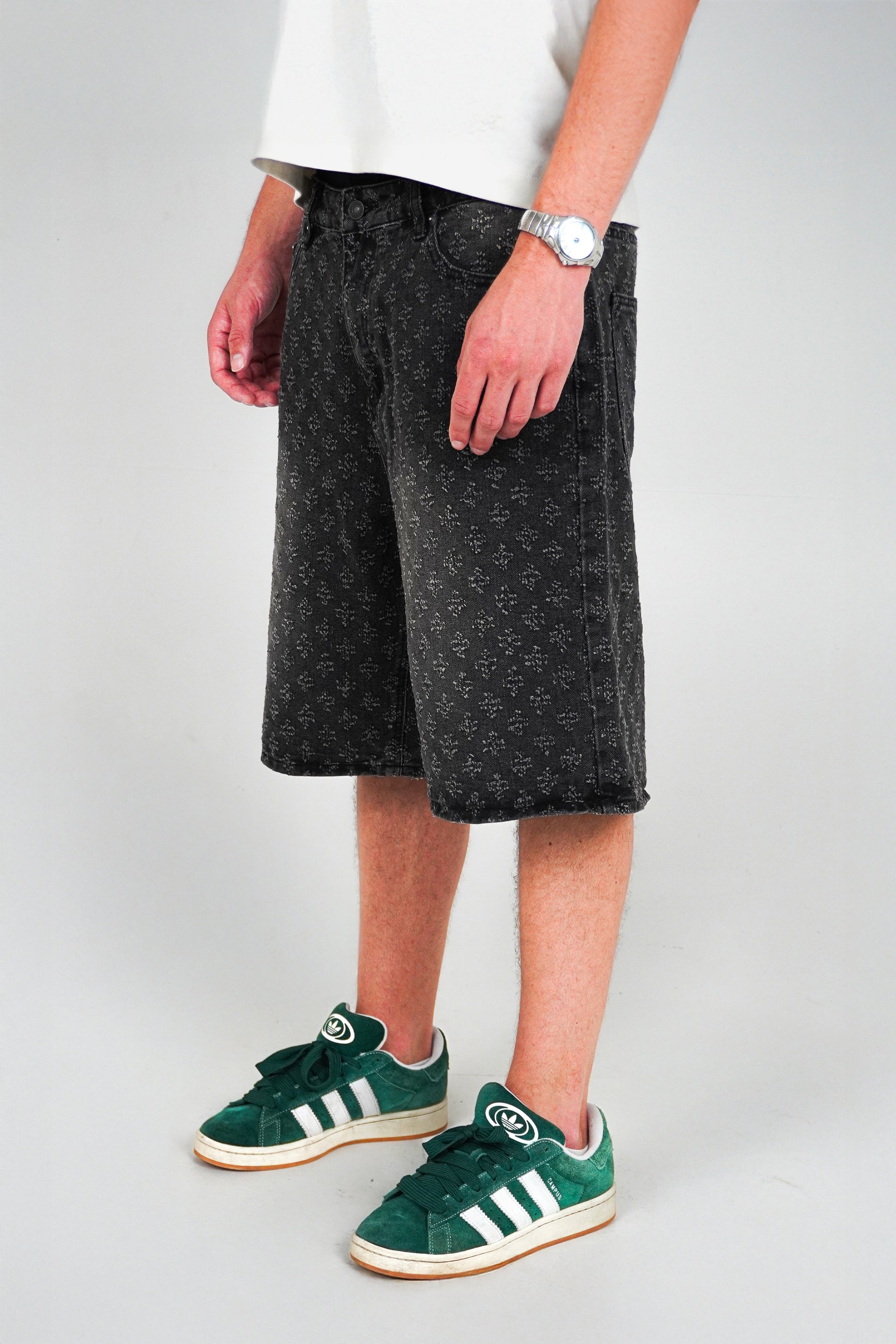 Person wearing black shorts and green Adidas sneakers on a plain background