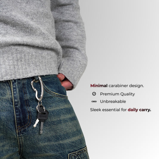 Persoon met een grijze trui en blauwe spijkerbroek met een sleutelhanger, op een lichtgrijze achtergrond.