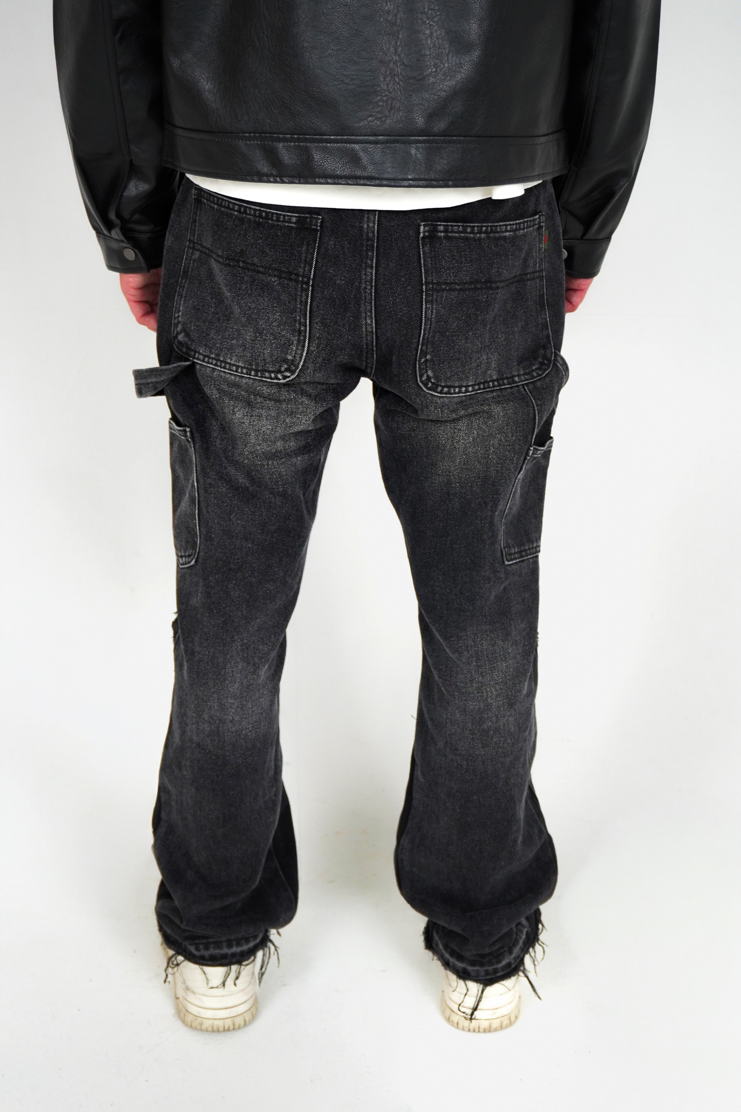Person wearing black leather jacket and dark jeans on a white background