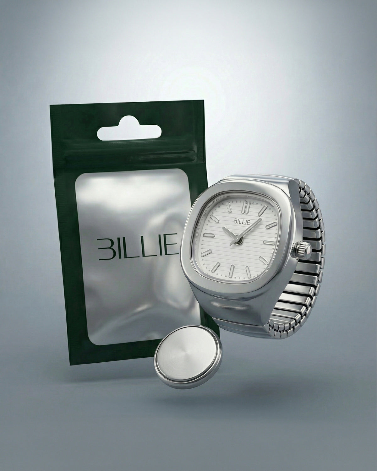 Billie Mono Ring Watch in silver with a white dial next to its Billie pouch packaging and spare battery