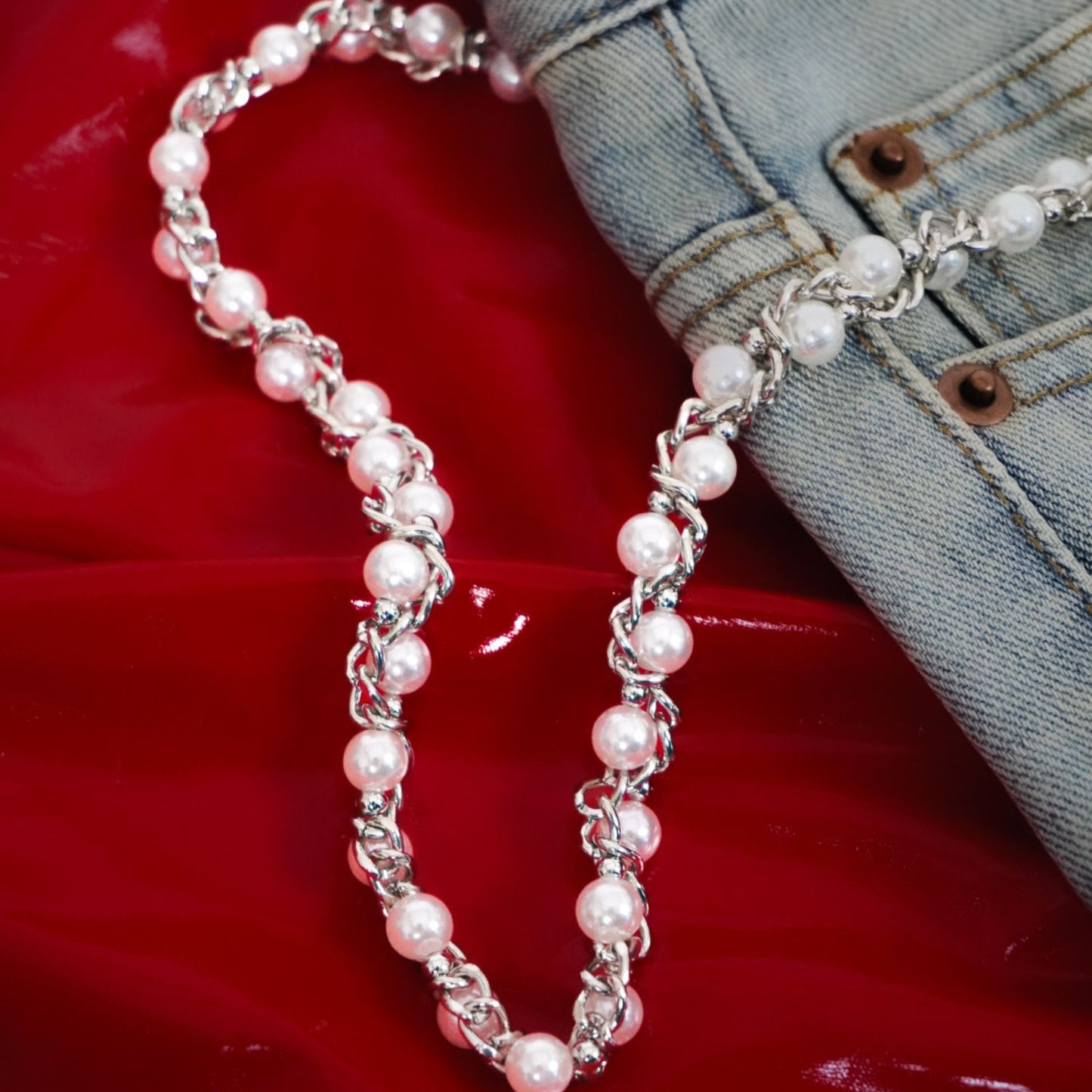 Pearl necklace draped over a denim jacket on a red surface