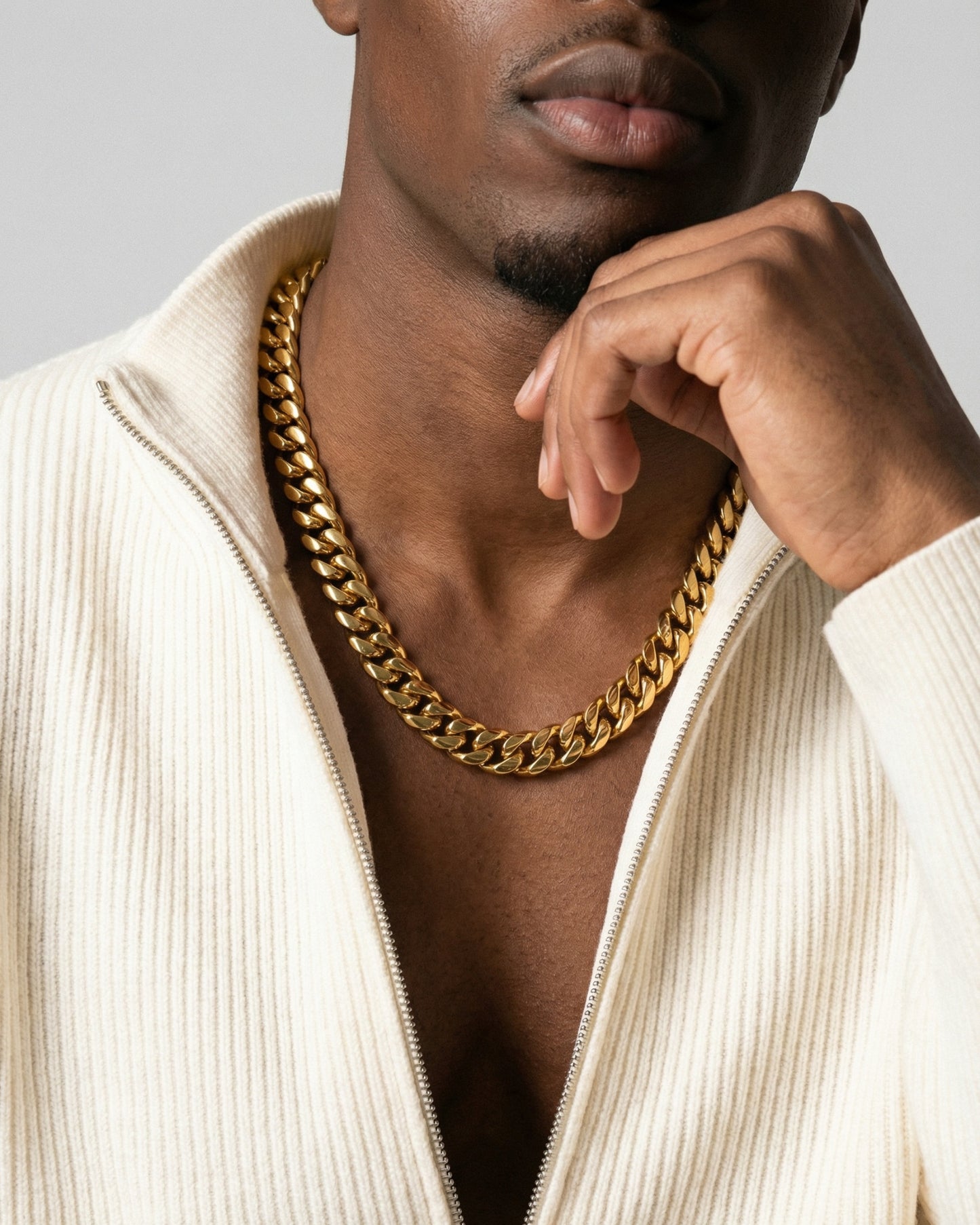Close-up of a person wearing a gold chain and a light-colored zip-up sweater.