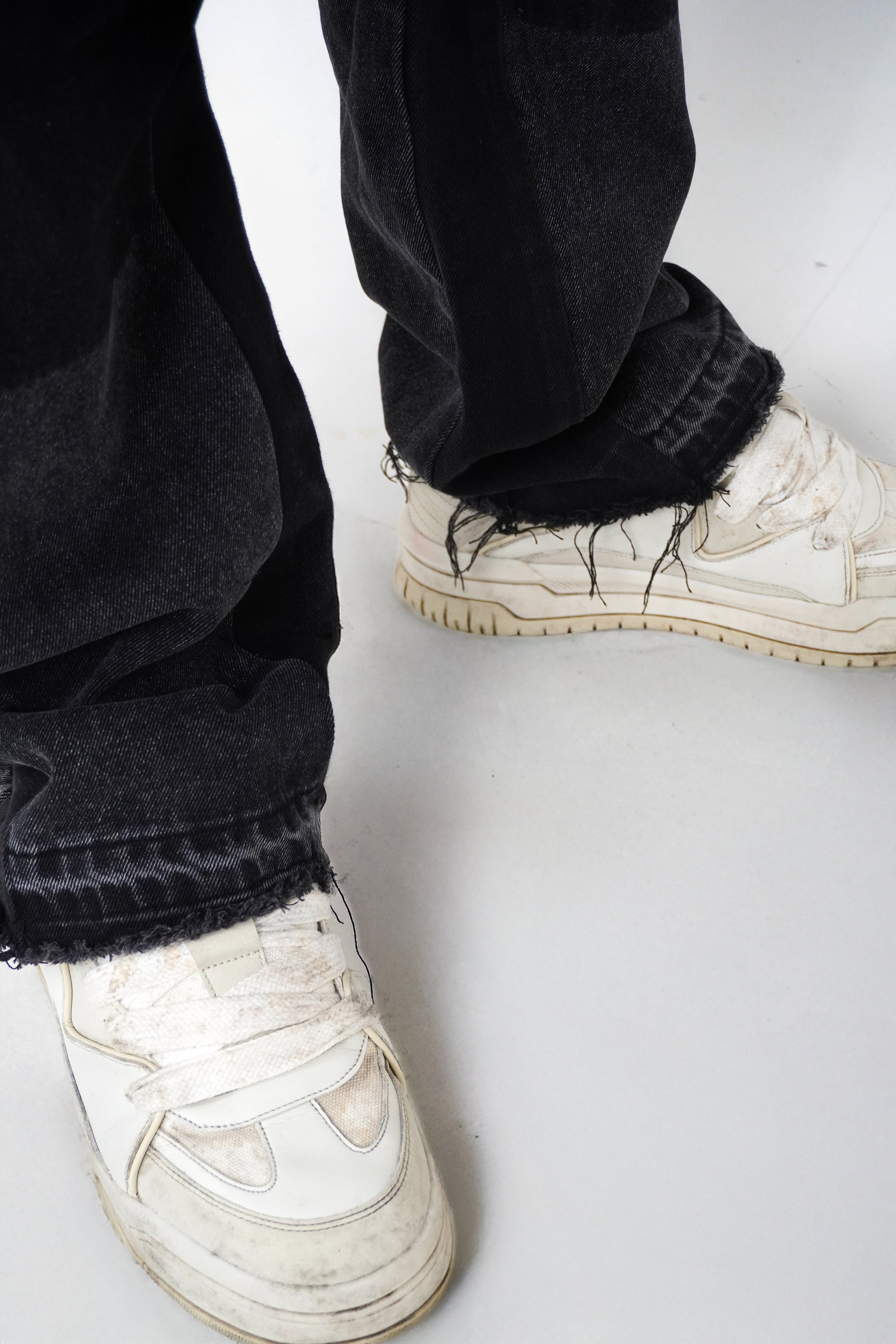 White sneakers worn with black pants on a white background