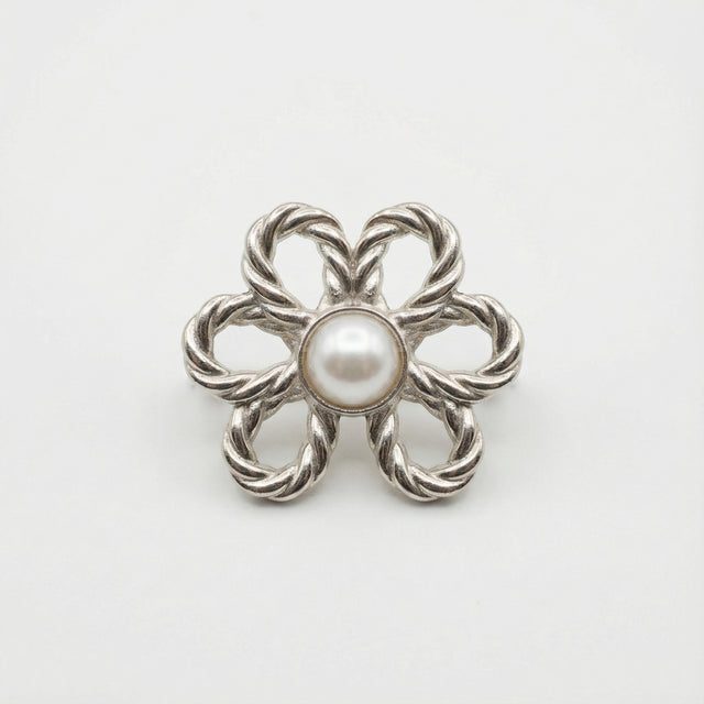 Silver brooch with a central pearl on a white background