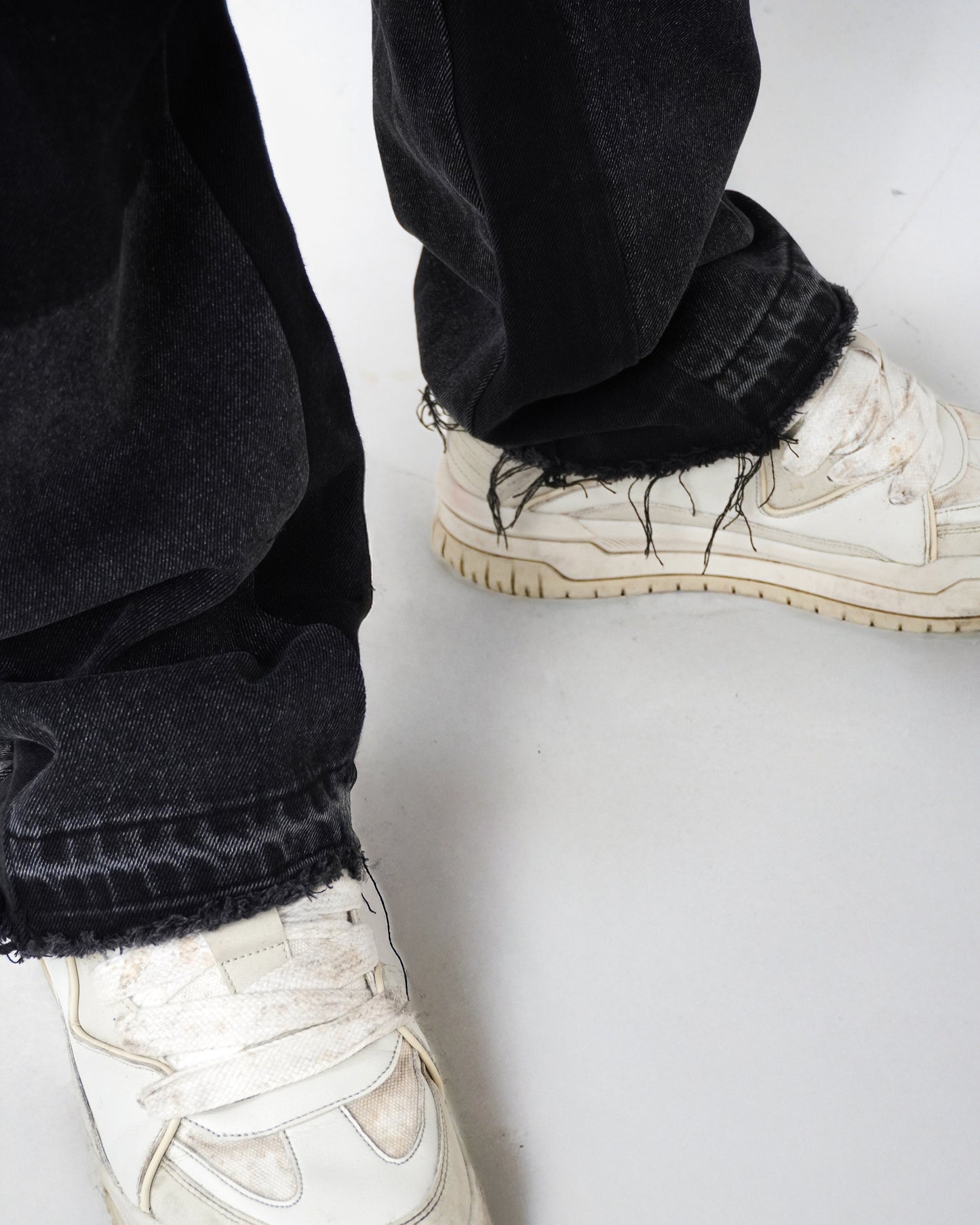 Black pants with frayed hem and white sneakers on a light background.