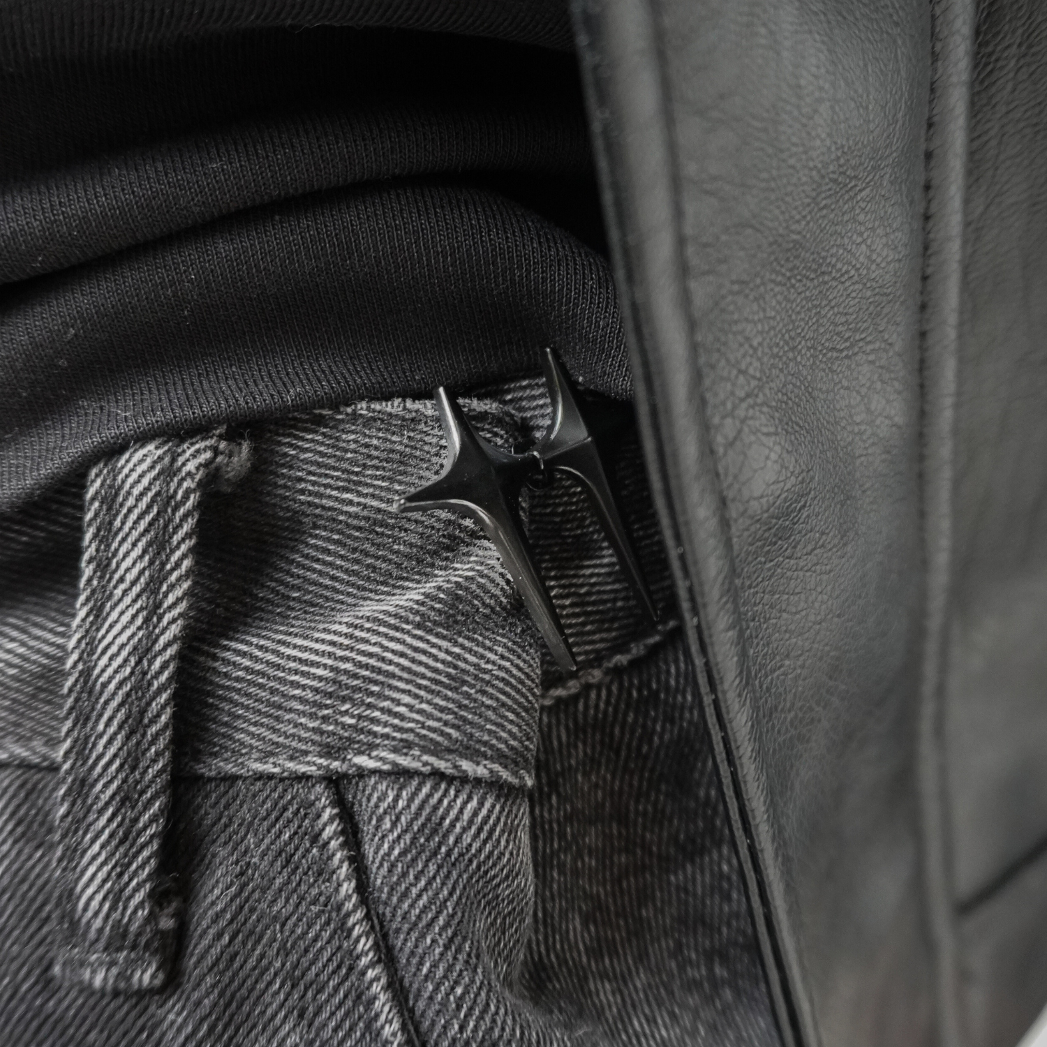 Close-up of a leather jacket with a button and belt buckle detail.