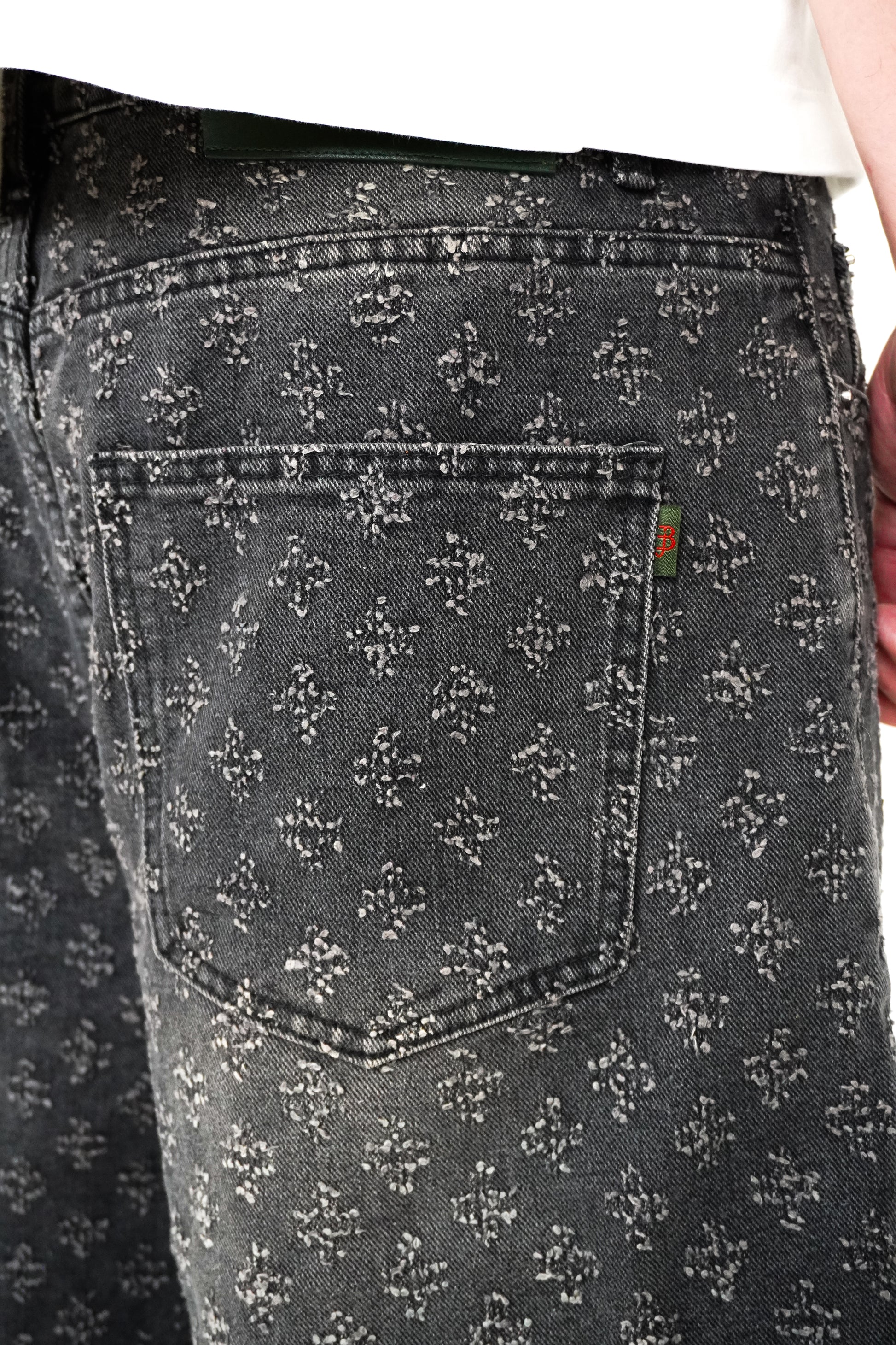 Close-up of a person wearing black patterned jeans with a brand logo on the pocket.