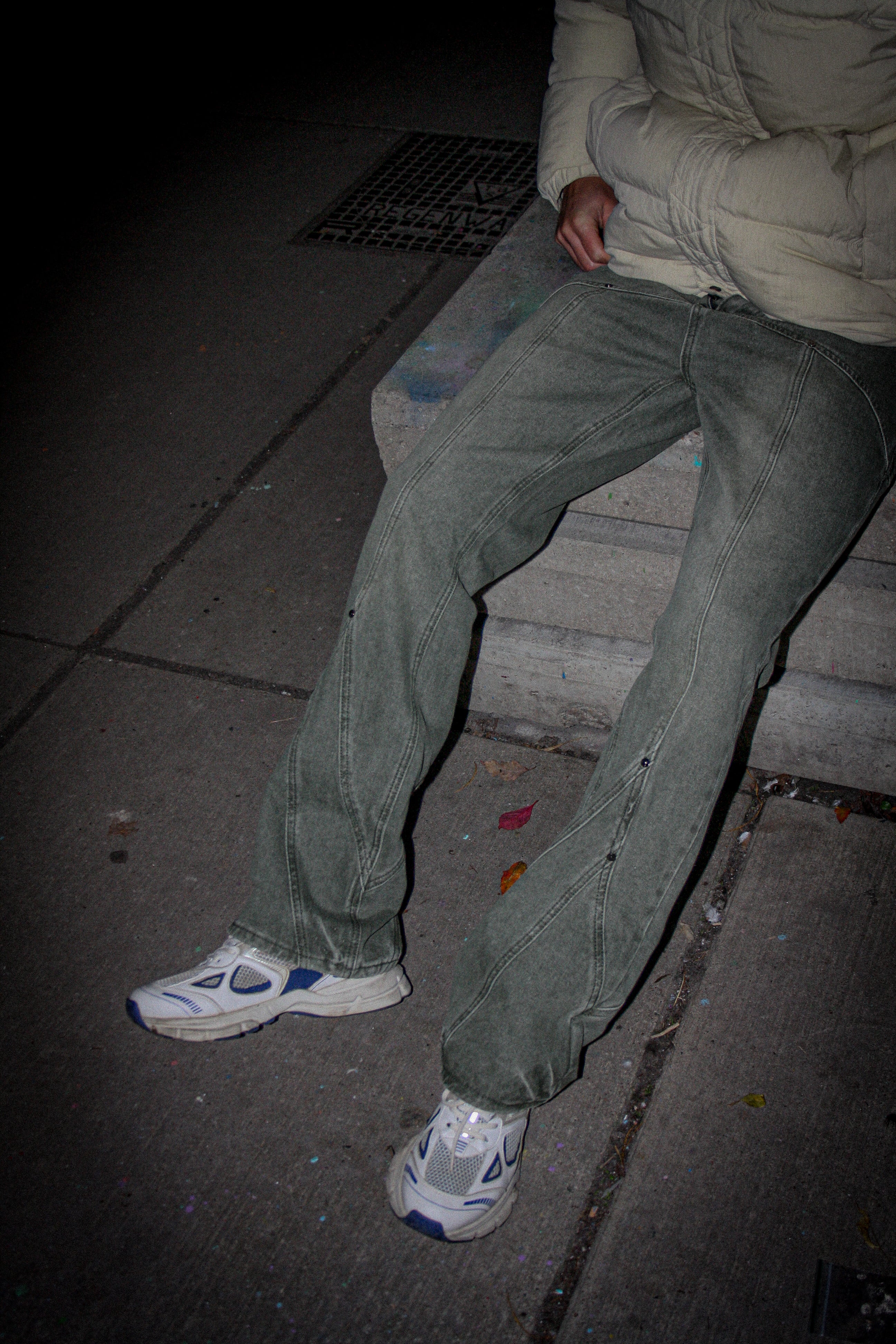 Person sitting on a step wearing green pants and white sneakers at night.