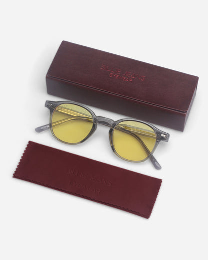Gray sunglasses with yellow lenses on a plain background with a maroon case and cleaning cloth.