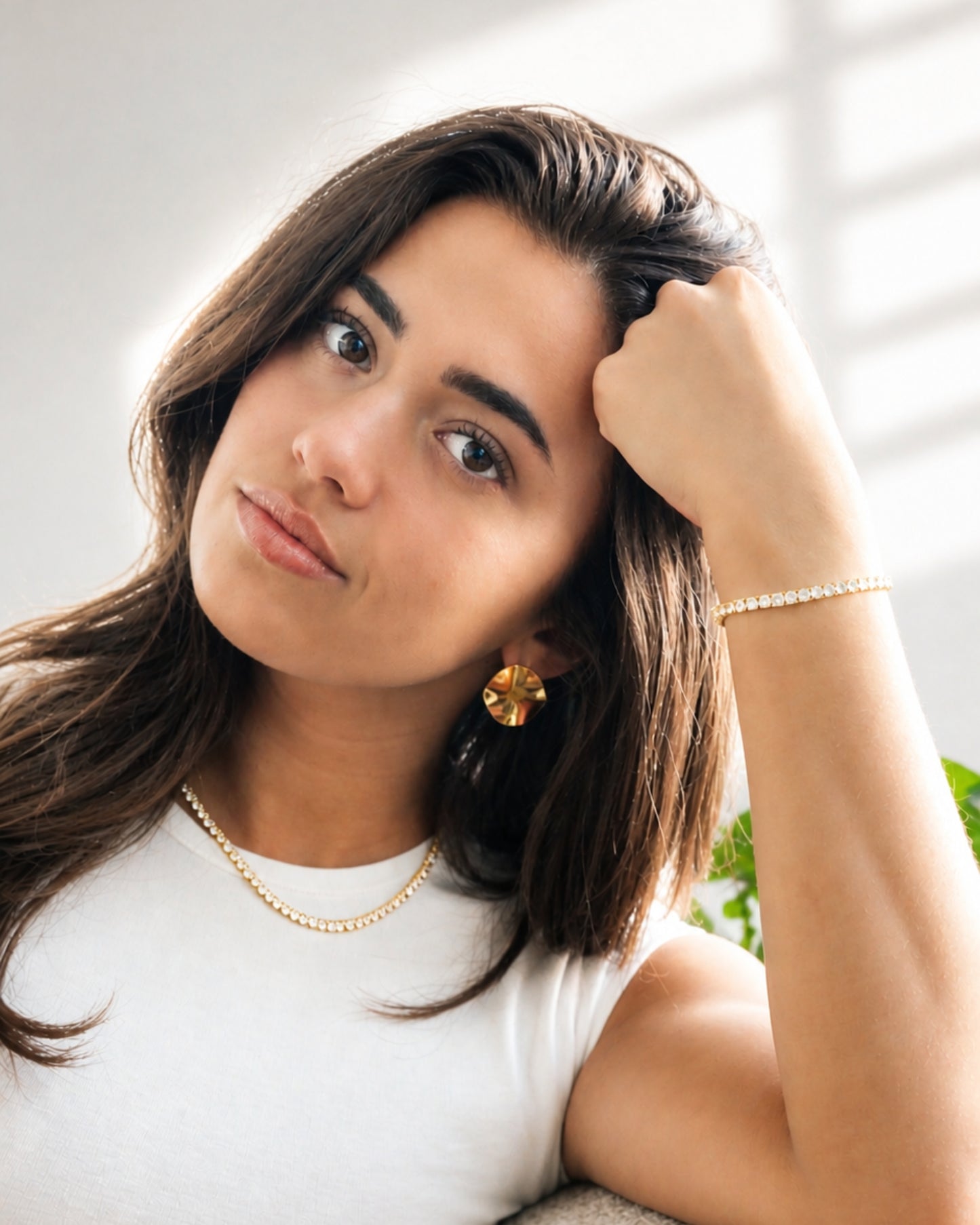 Person with long hair wearing earrings and a necklace, resting their head on their hand.
