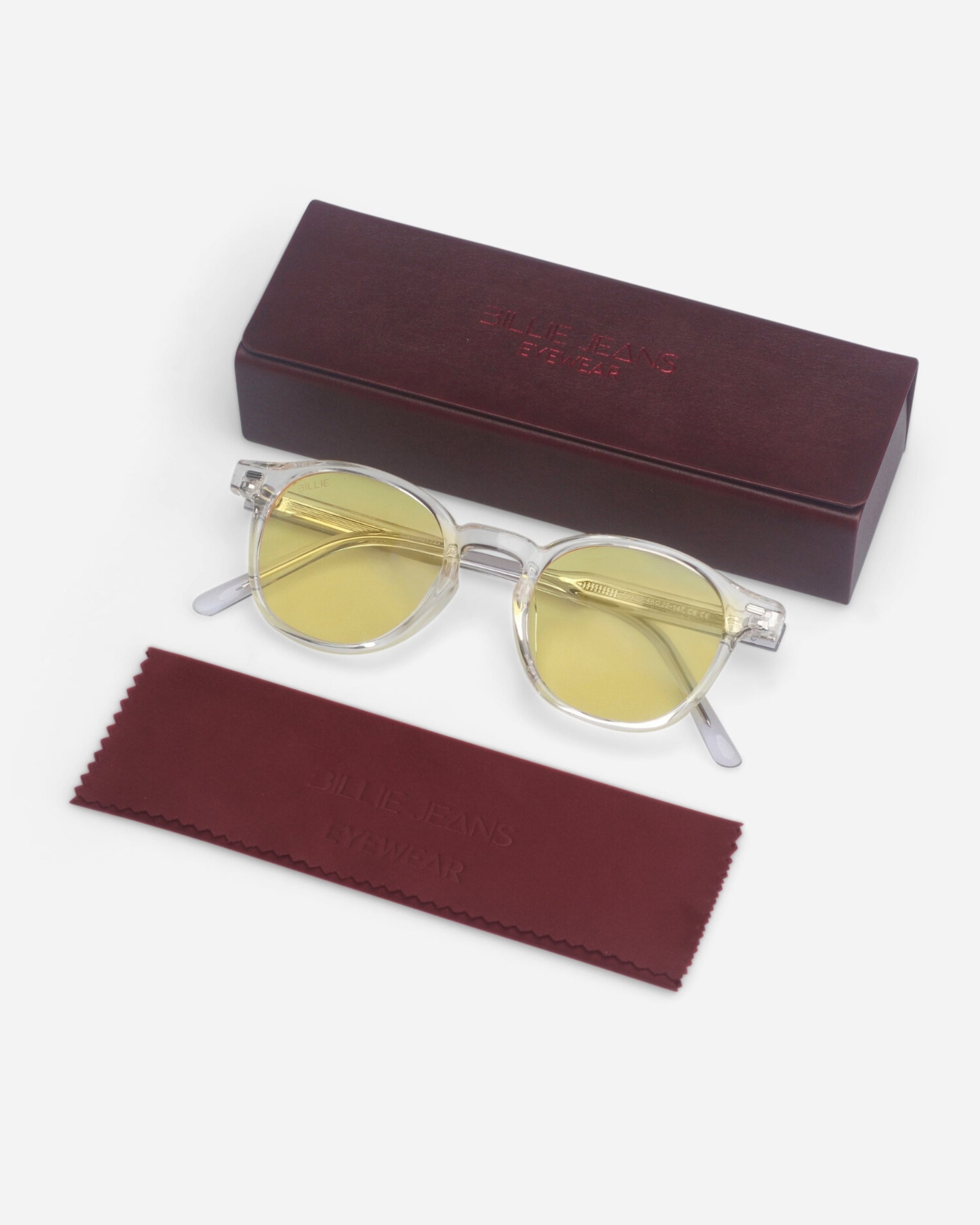 Round yellow-tinted sunglasses on a plain background with a maroon case and cleaning cloth.