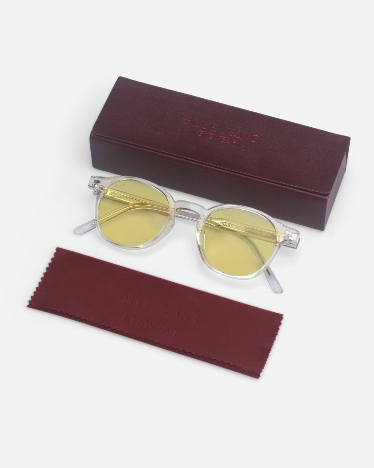 Billie Blue Light Glasses in clear with yellow lenses next to the burgundy case and cleaning cloth