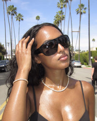 Woman in sunglasses wearing the gold Billie Tennis Bracelet 4mm and tennis chain between palm trees