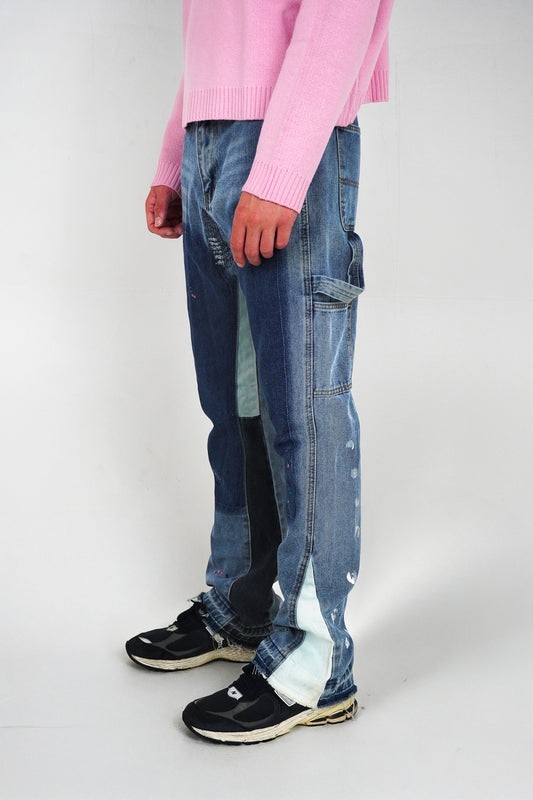 Person wearing a pink sweater, blue patchwork jeans, and black shoes on a white background
