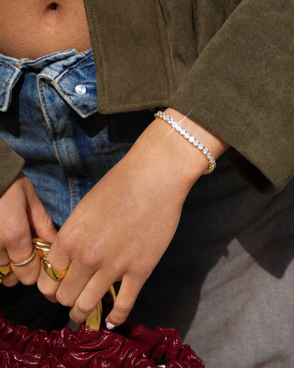 Close-up of a hand holding a burgundy bag, wearing a gold bracelet and rings.