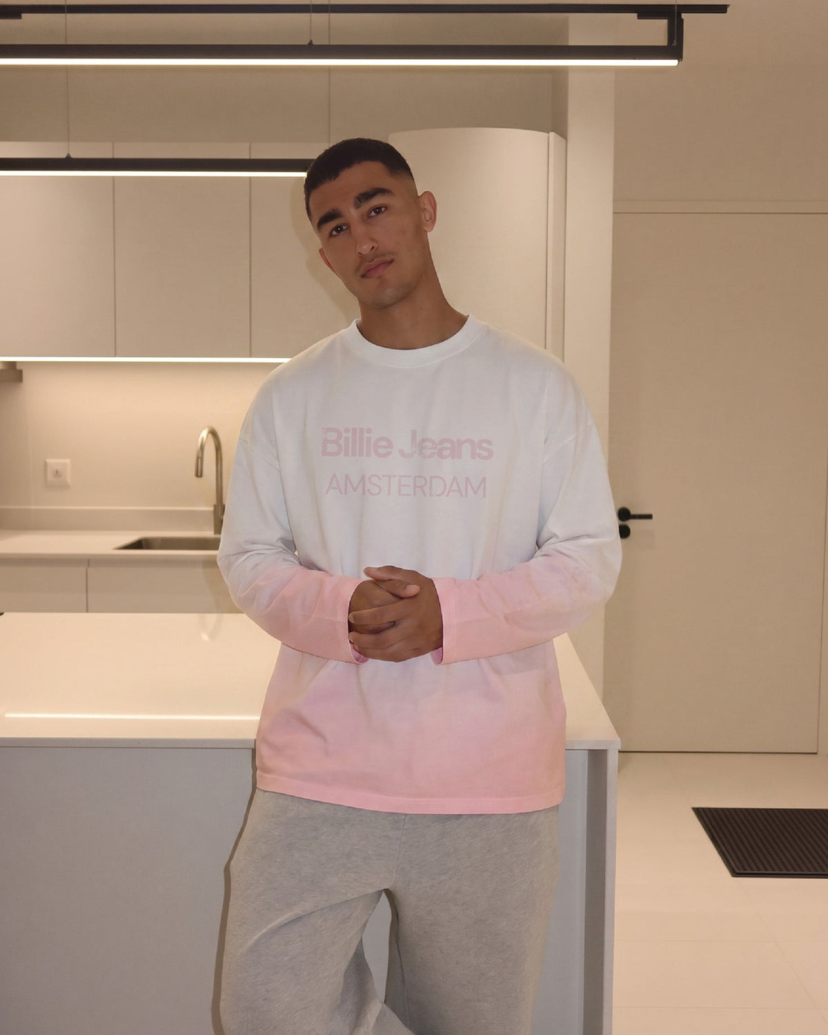 Man wearing the Billie Long Sleeve Fade with grey sweatpants in a kitchen