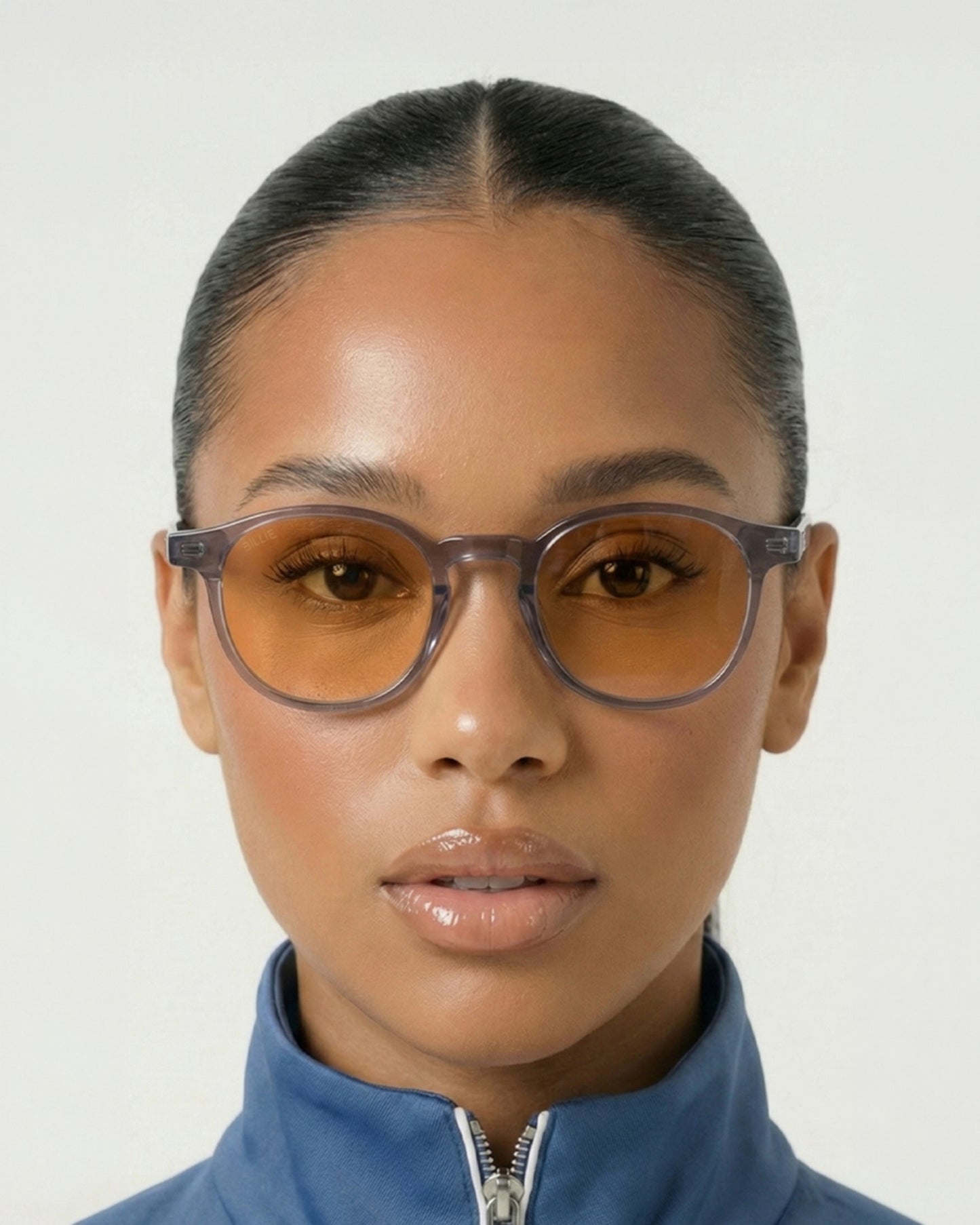 Person wearing orange-tinted glasses and a blue zip-up jacket, with a neutral background.
