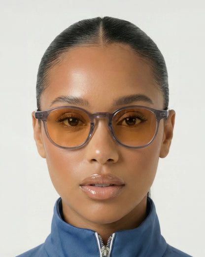 Person wearing orange-tinted glasses and a blue zip-up jacket, with a neutral background.