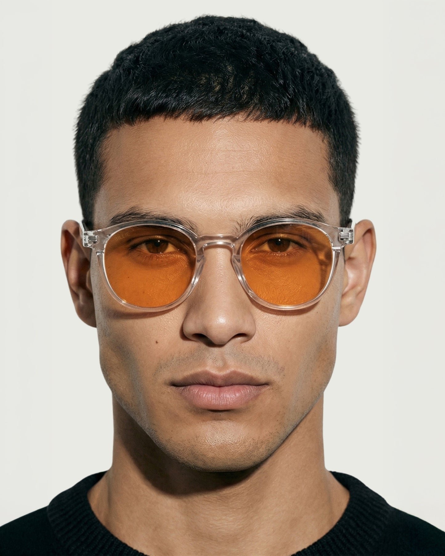 Person wearing clear-framed sunglasses with orange lenses, facing forward.