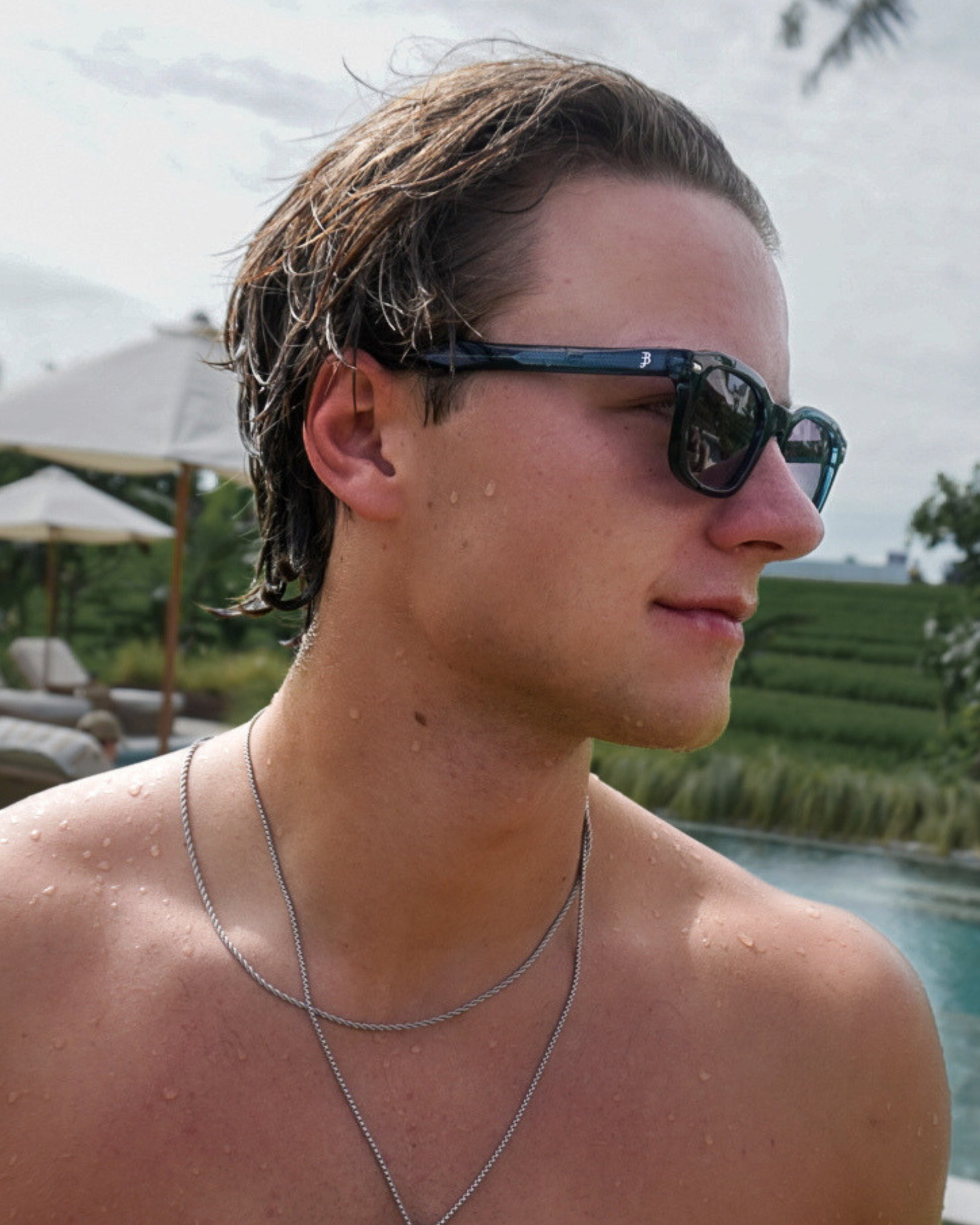 Profile of a person with wet hair and sunglasses, droplets on skin, outdoor setting