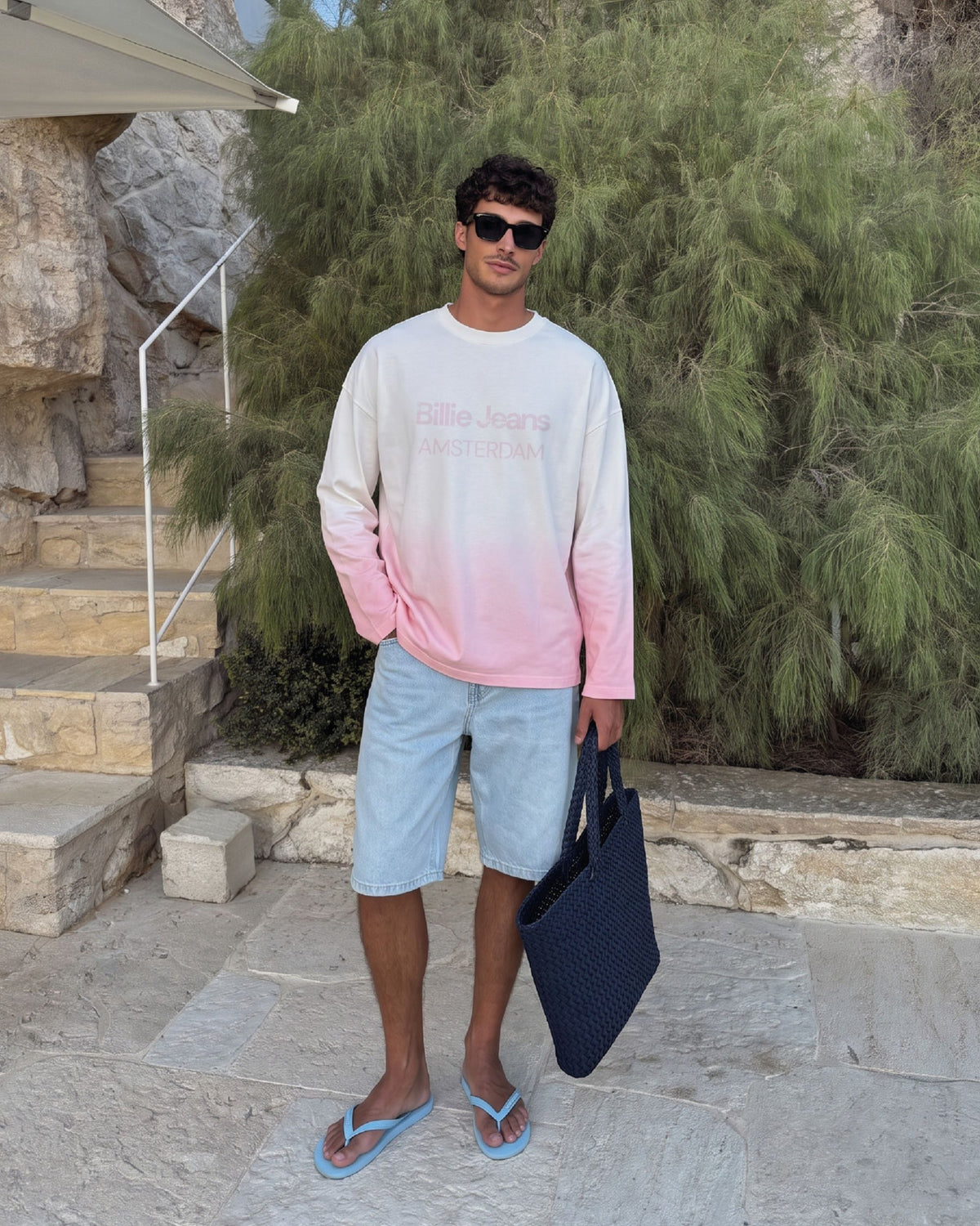 Man wearing the Billie Long Sleeve Fade with denim shorts on a garden staircase