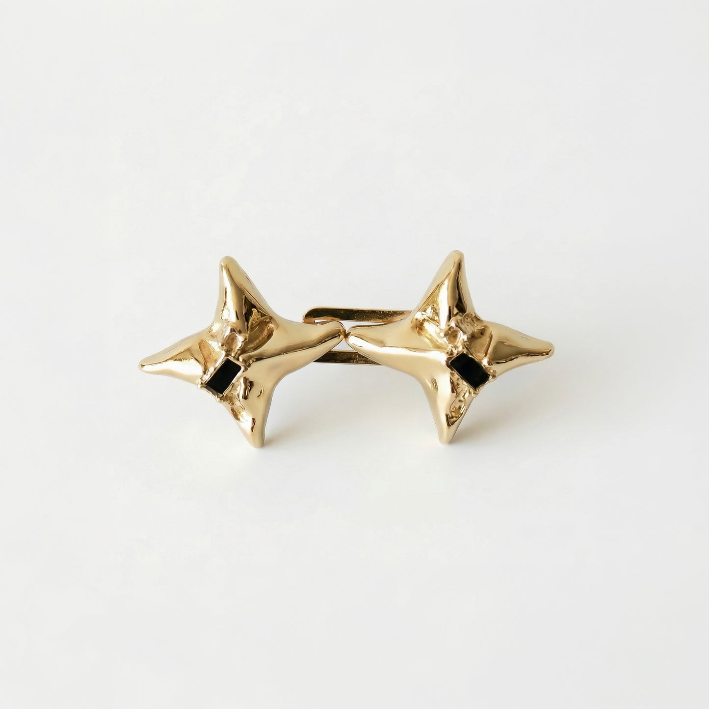 Gold star-shaped earrings with black centers on a white background