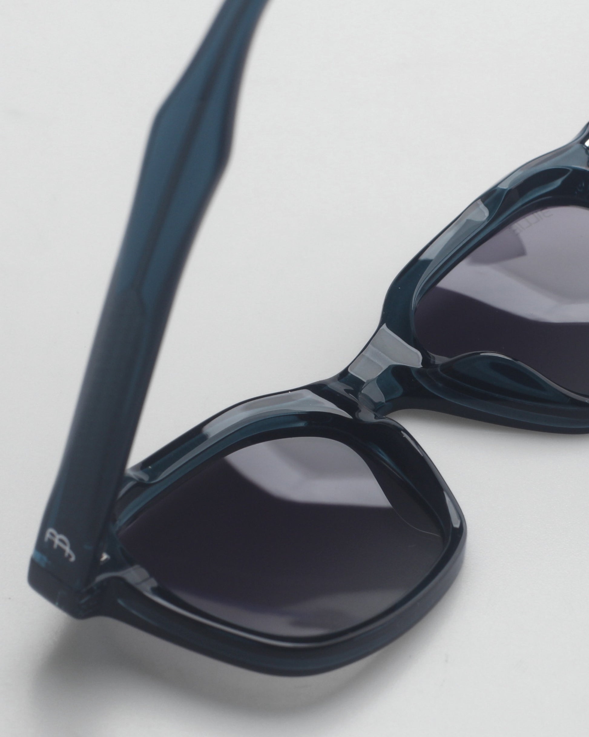 Close-up of dark sunglasses with a glossy frame on a light background.