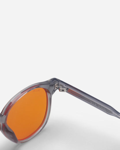Side view of sunglasses with orange lenses and clear frames on a plain background.