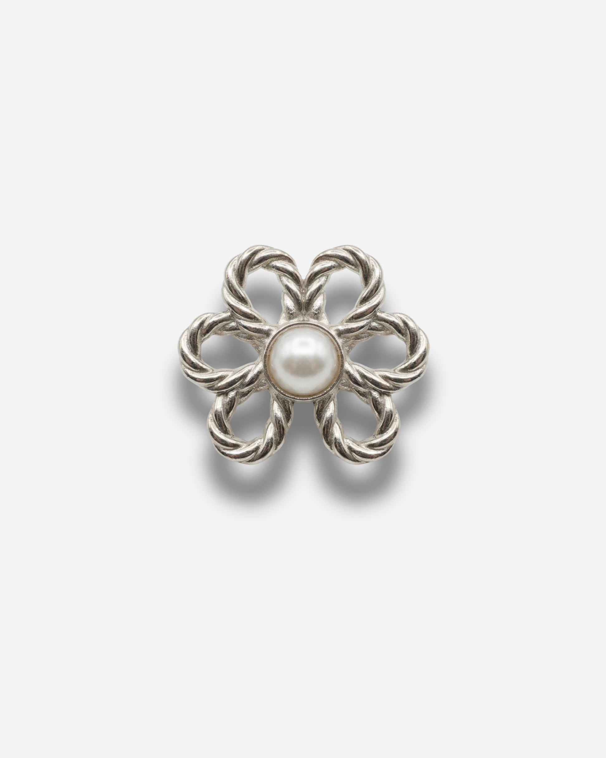 Silver flower-shaped brooch with a central pearl on a plain background.