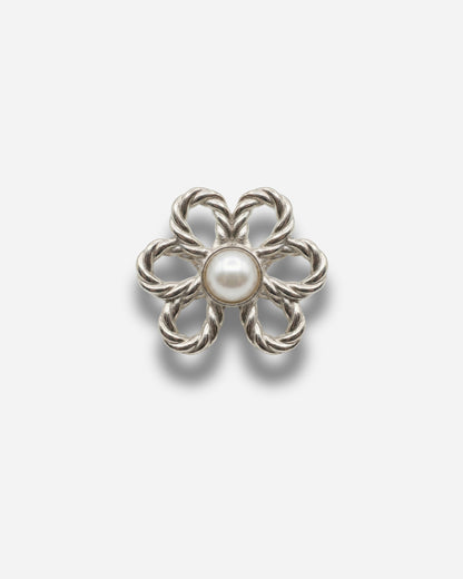 Silver flower-shaped brooch with a central pearl on a plain background.