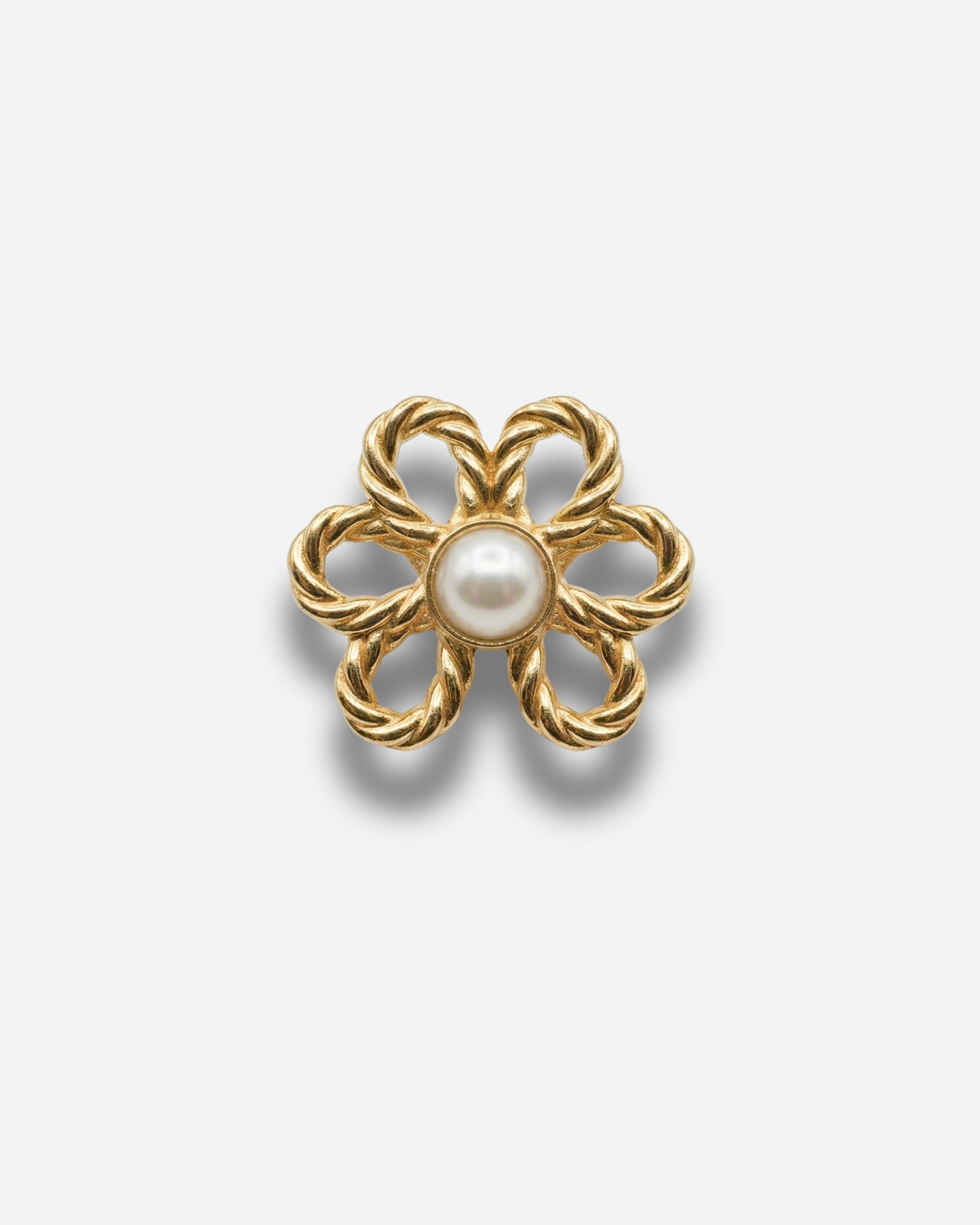 Gold flower-shaped brooch with a pearl center on a plain background.