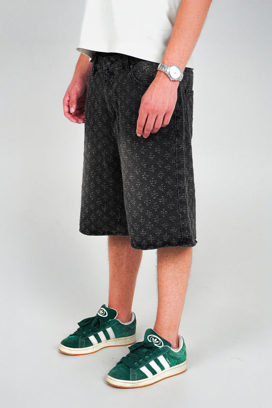 Person wearing black shorts and green Adidas sneakers on a plain background