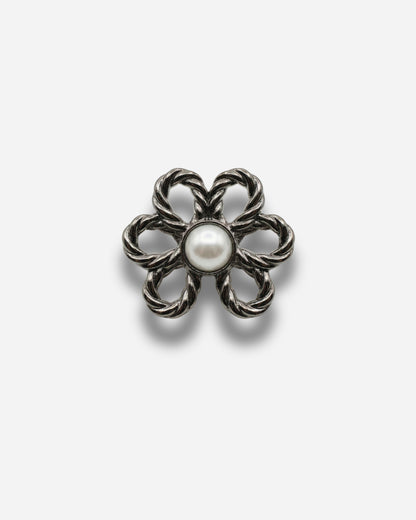 Flower-shaped brooch with a central pearl on a plain background.