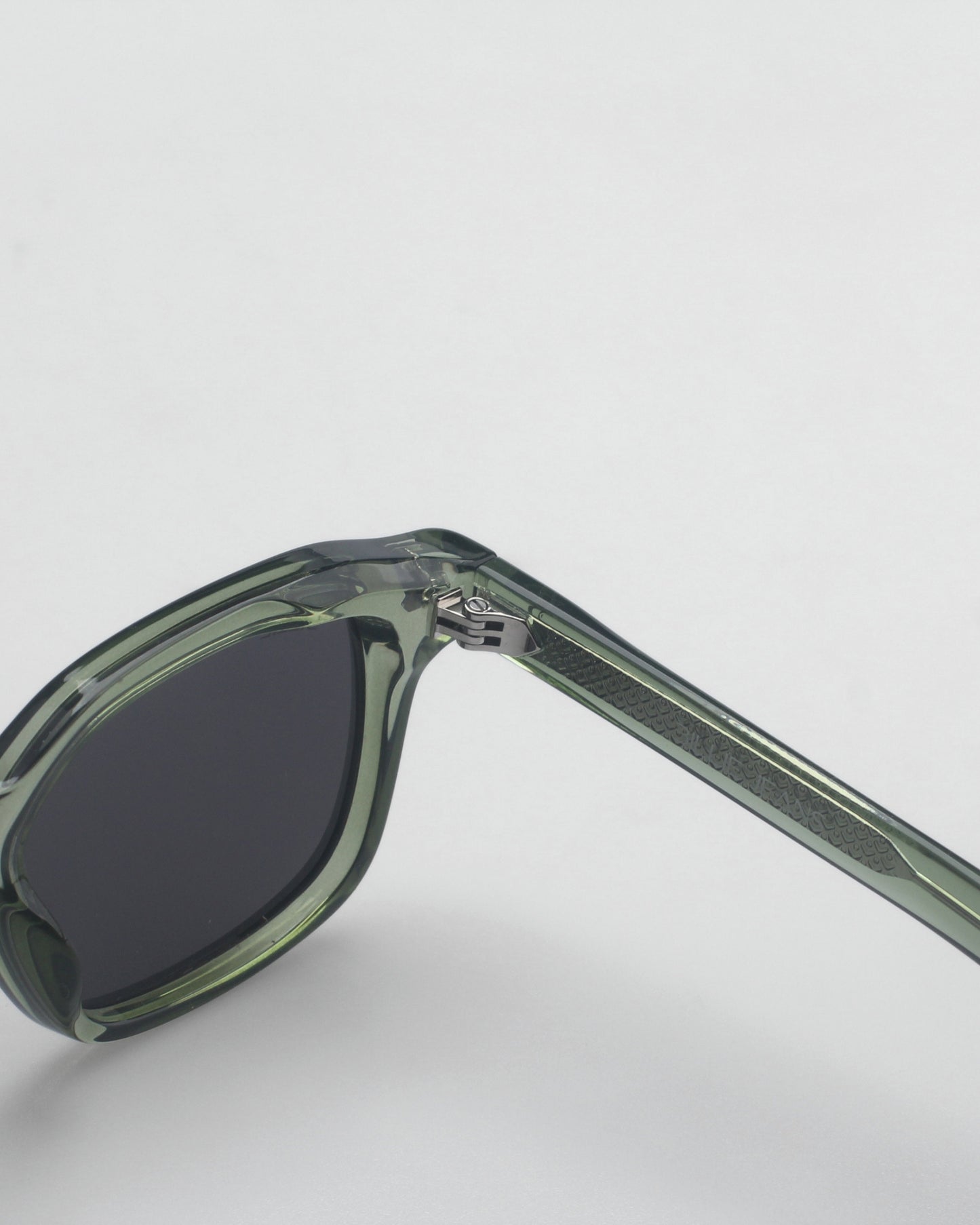 Close-up of green sunglasses with dark lenses and patterned temple on a plain background.