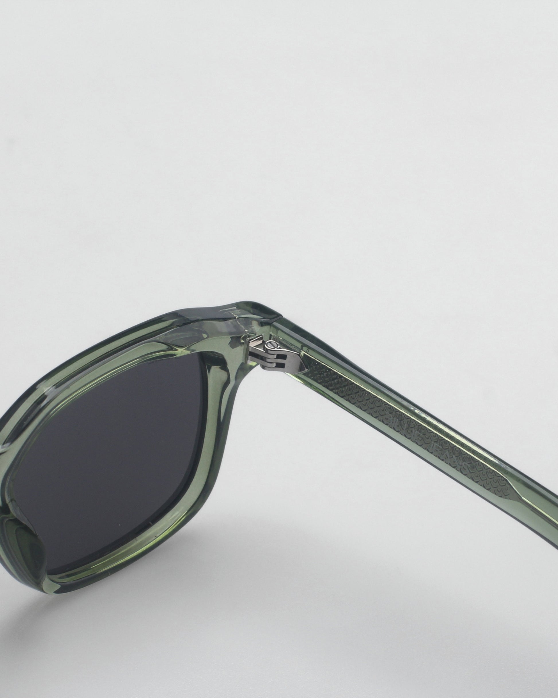 Close-up of green sunglasses with dark lenses and patterned temple on a plain background.