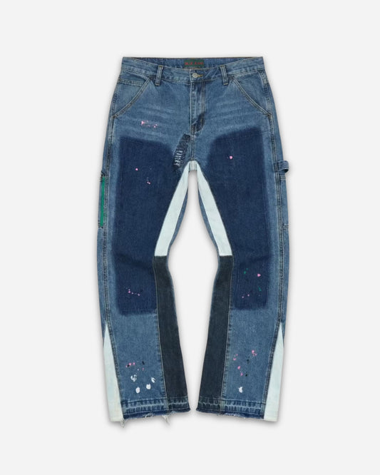 Patchwork jeans with various shades of blue and paint splatters, displayed on a plain background.