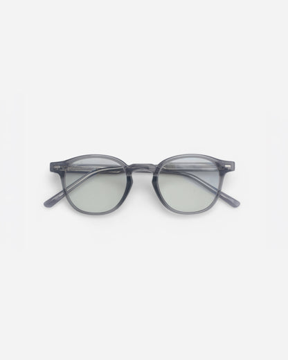 Round glasses with a transparent gray frame and light green lenses on a plain background.