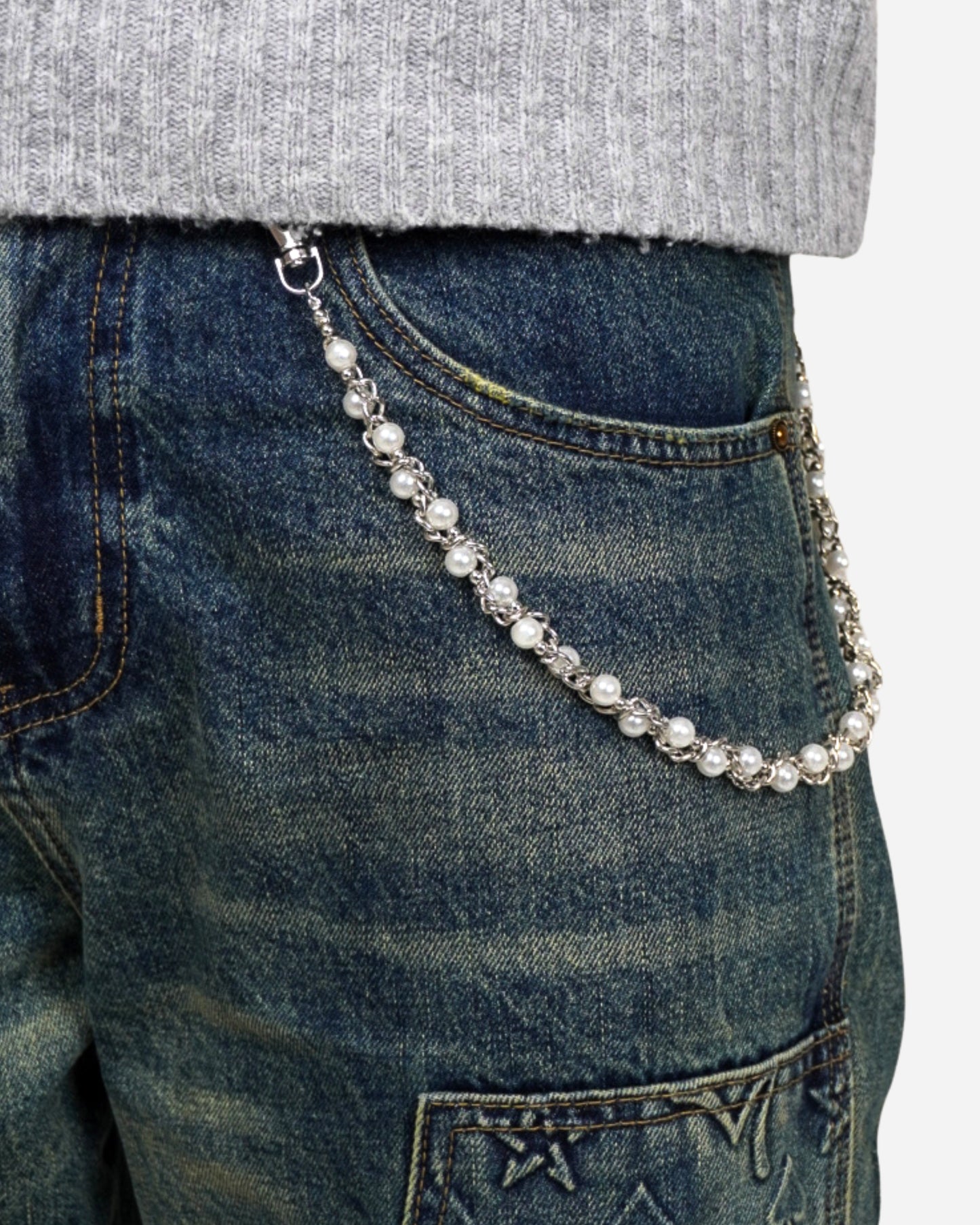 Close-up of a silver chain with pearls attached to the waistband of blue jeans.