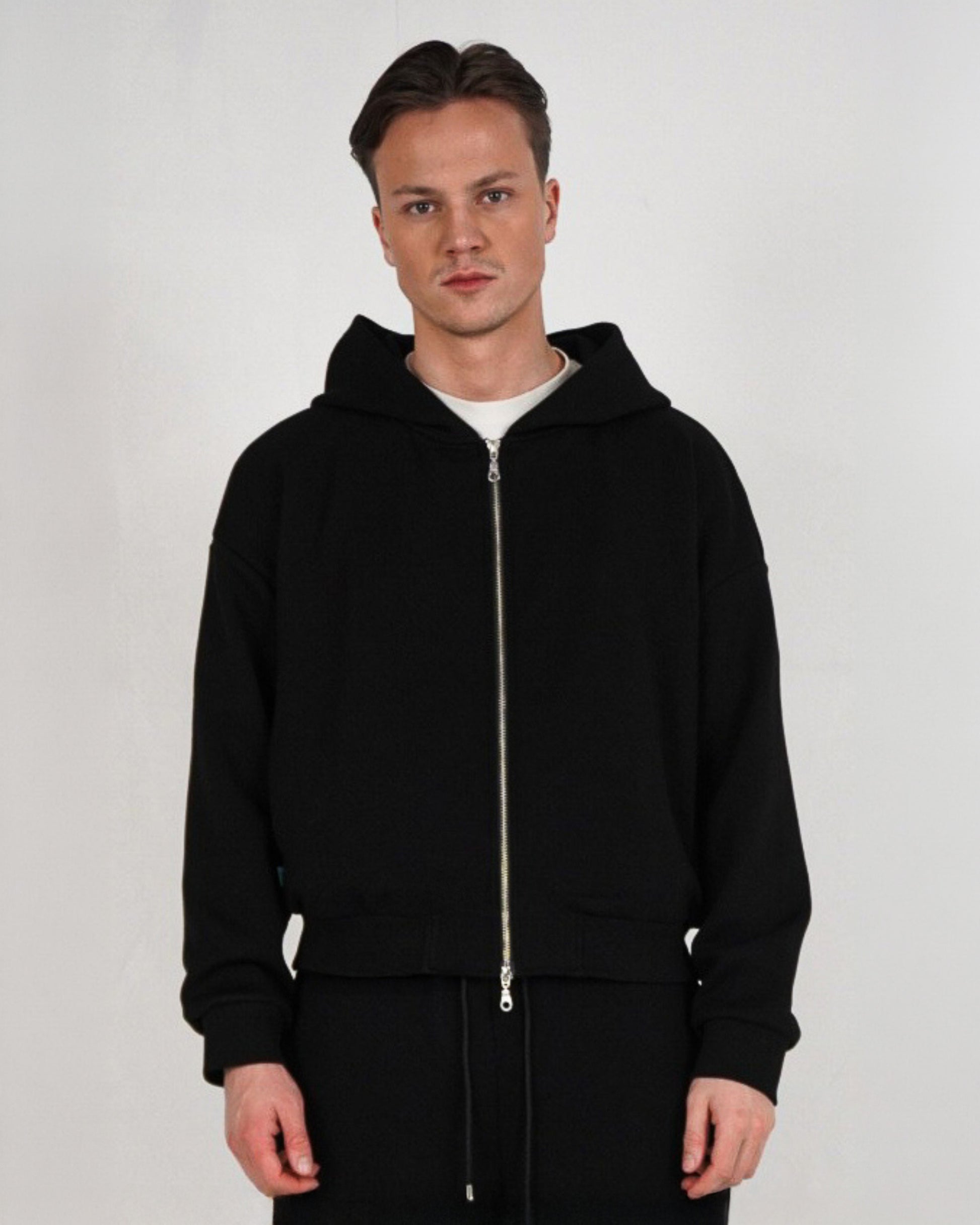 Person wearing a black zip-up hoodie with a white t-shirt underneath.