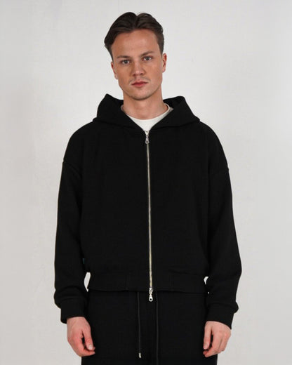 Person wearing a black zip-up hoodie with a white t-shirt underneath.
