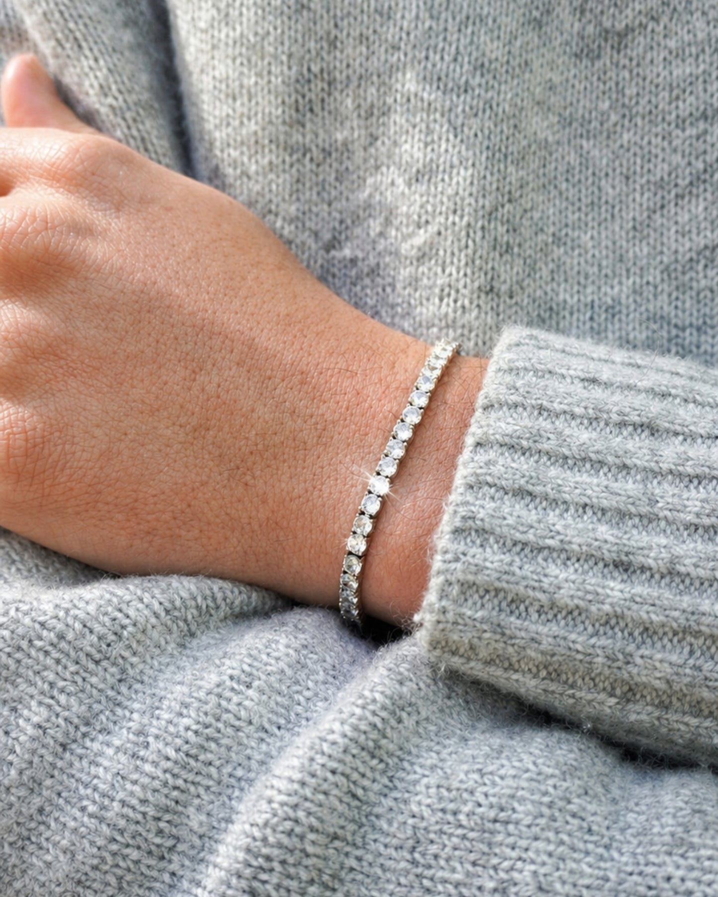 Close-up of a hand wearing a silver bracelet on a gray sweater.