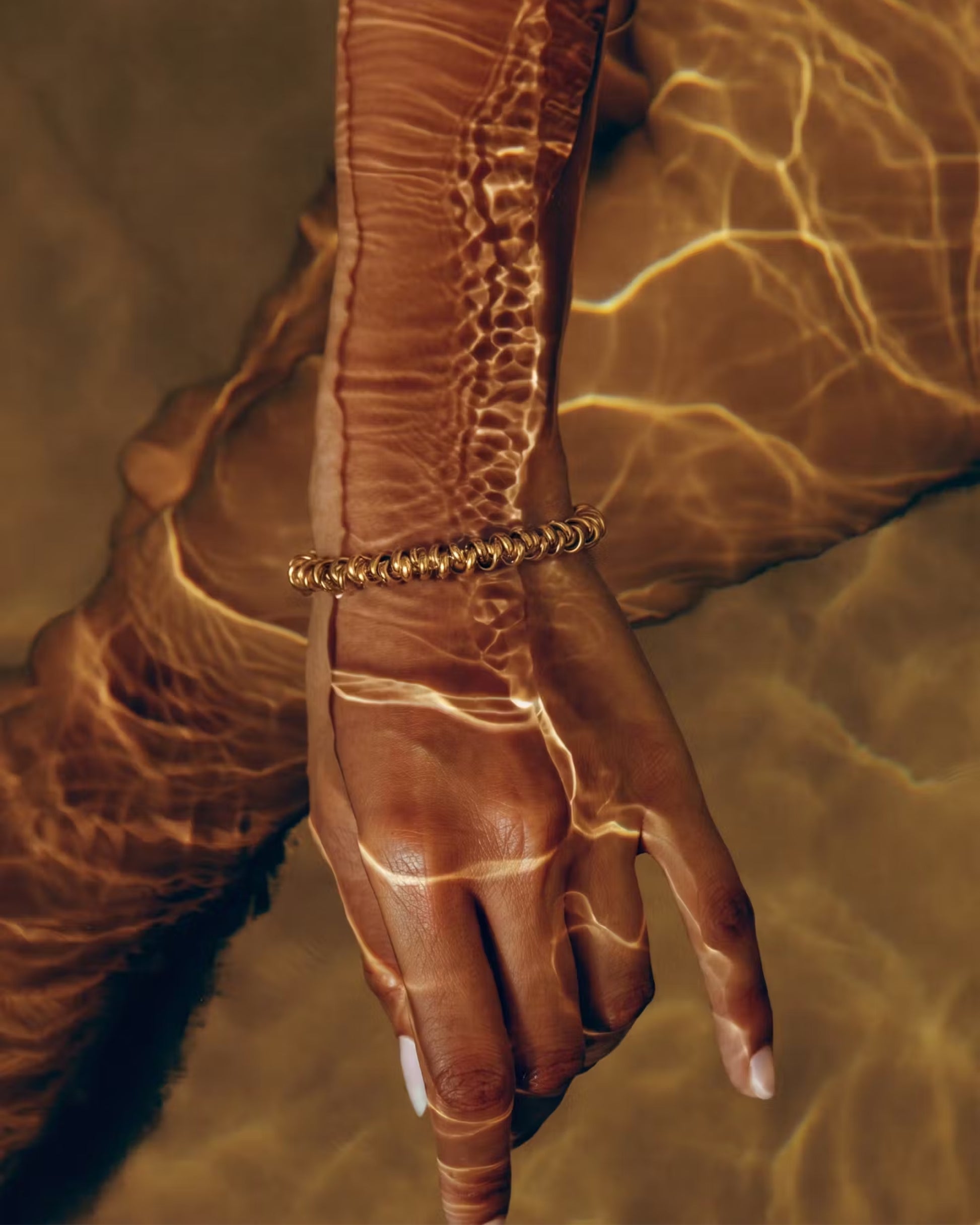 A hand submerged in water with light reflections creating patterns on the skin.