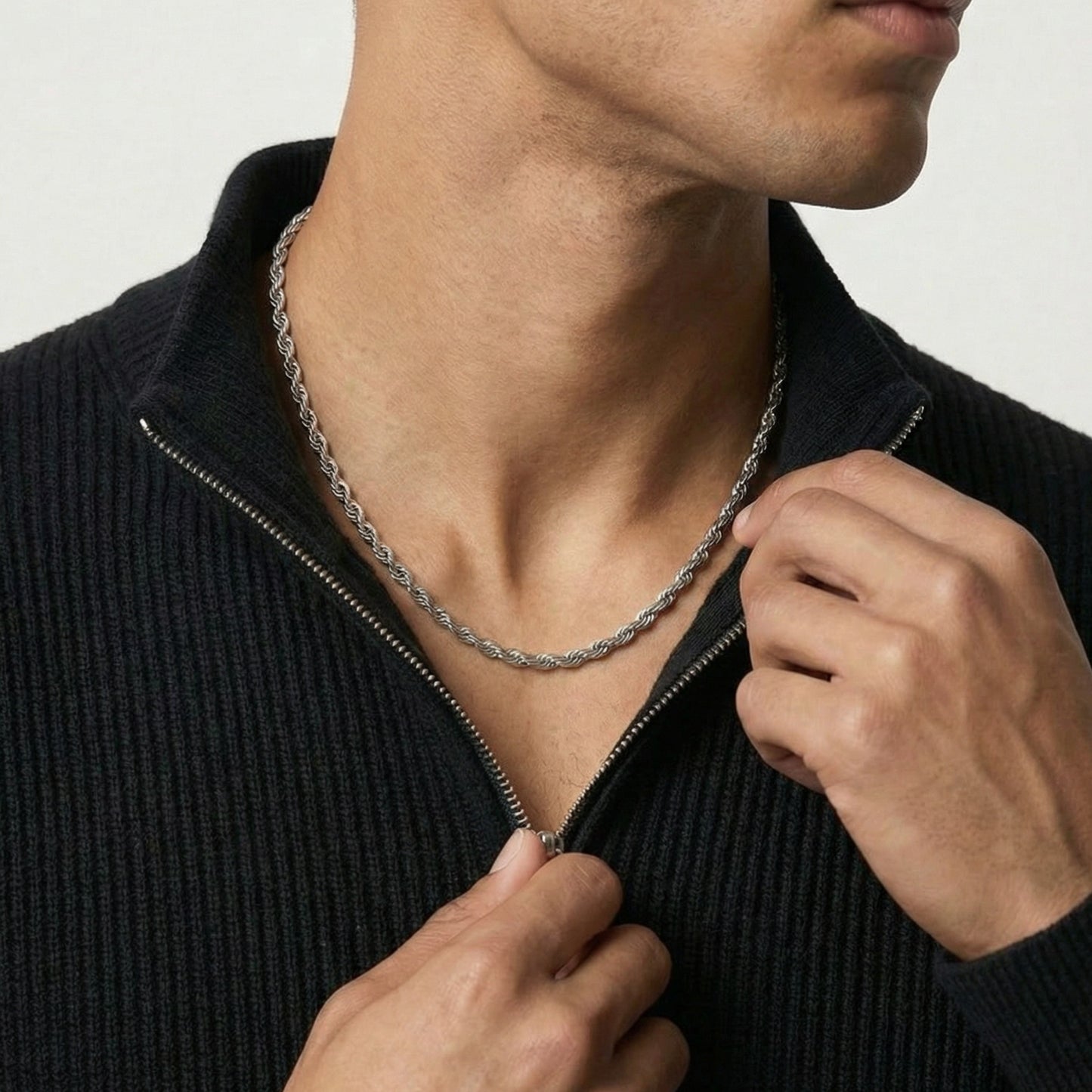 Person wearing a black sweater with a silver chain necklace against a neutral background