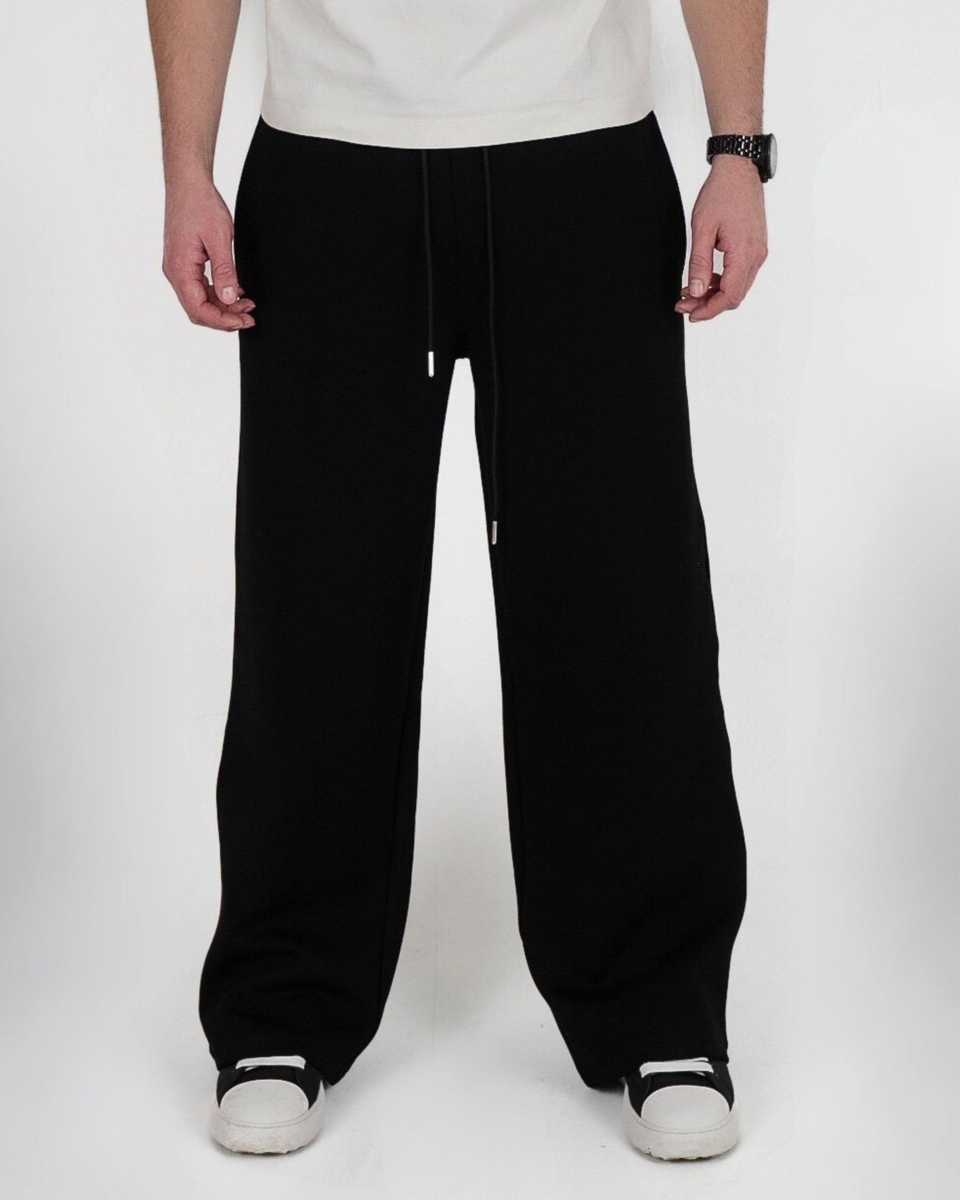 Person wearing black pants and white shoes, standing on a plain background.