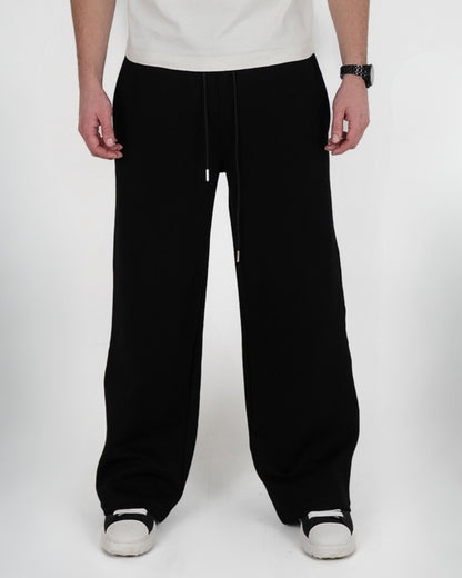 Person wearing black pants and white shoes, standing on a plain background.