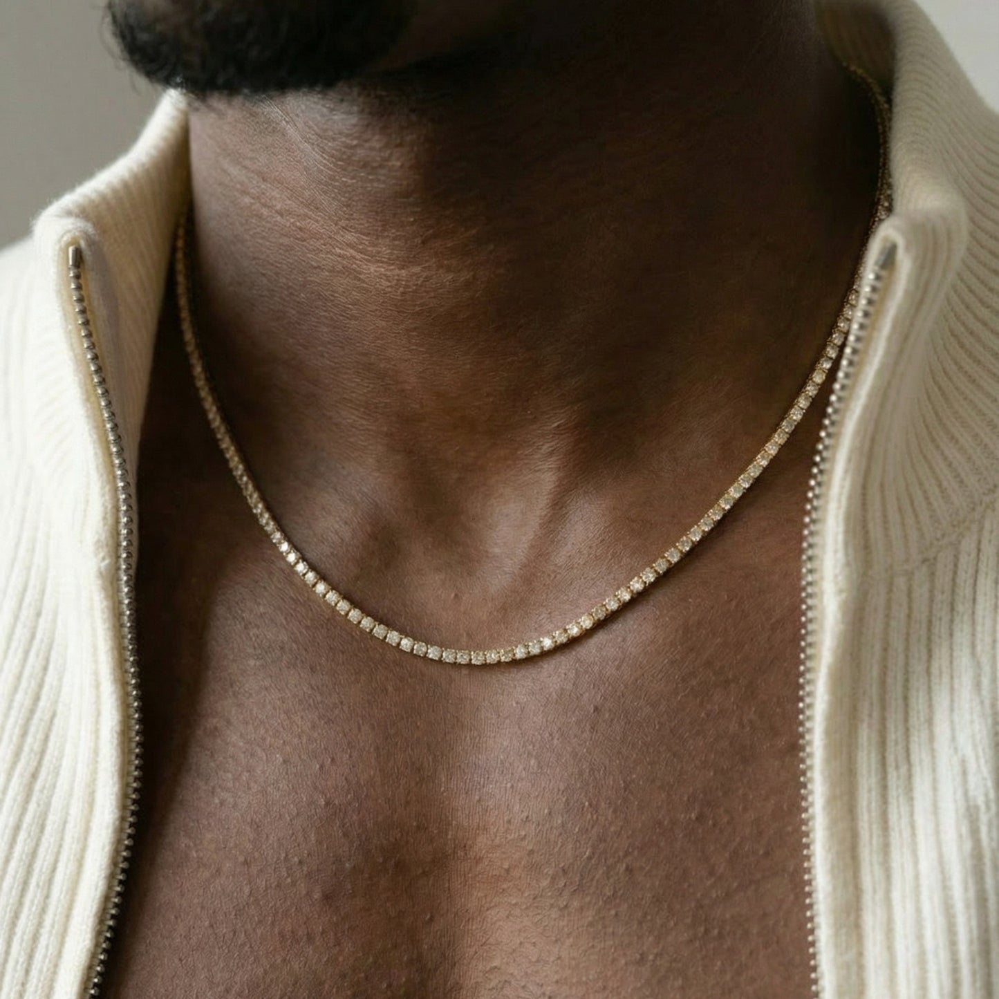 Close-up of a person wearing a gold chain necklace with a neutral background